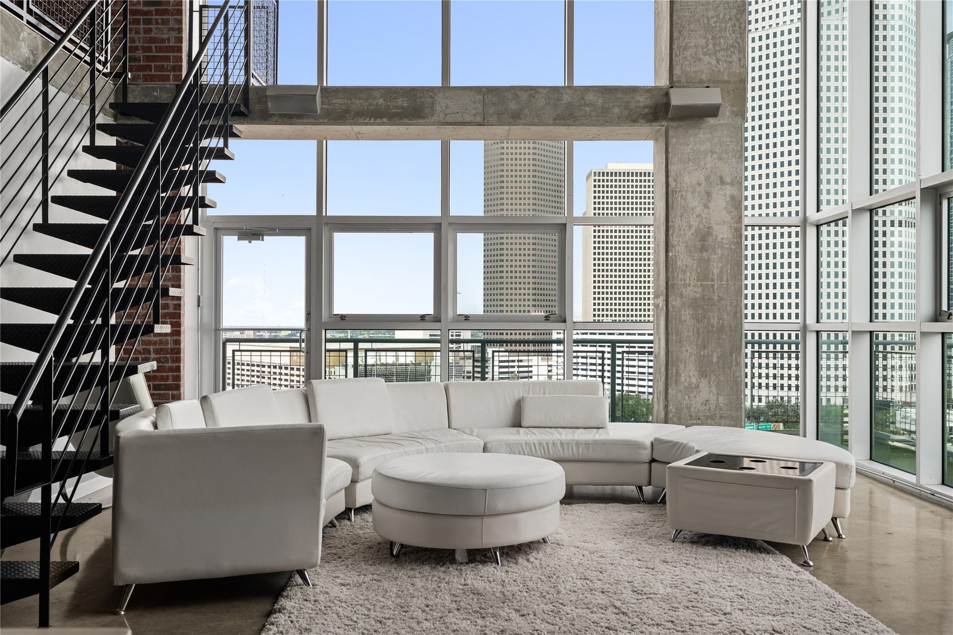 The dramatic two story living room is framed by floor to ceiling windows, filling the space with natural light while showcasing the scale and architectural character of the loft.