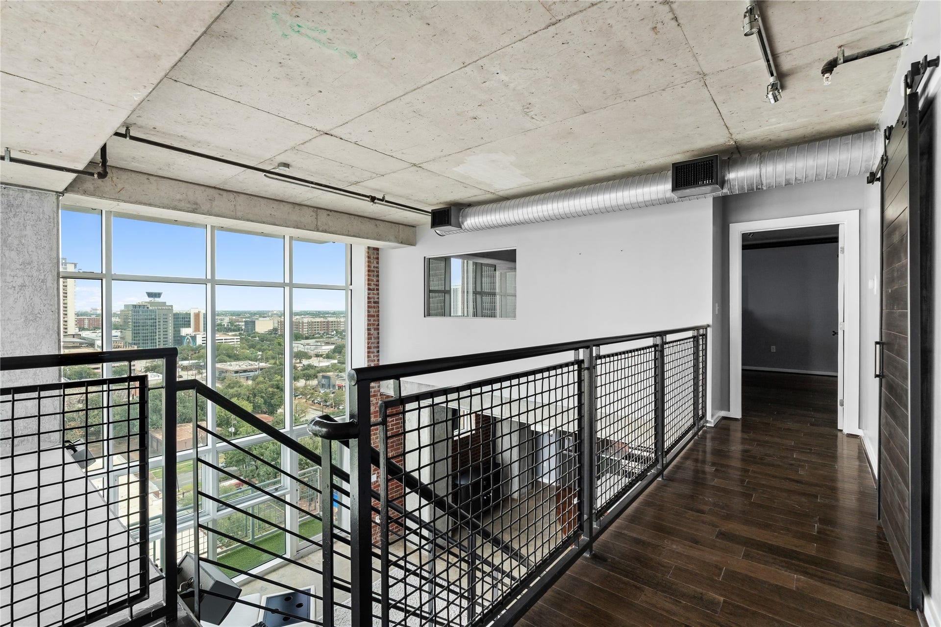 The upper level overlooks the dramatic two story living space, with exposed concrete, open railings and expansive windows reinforcing the homes authentic loft character.