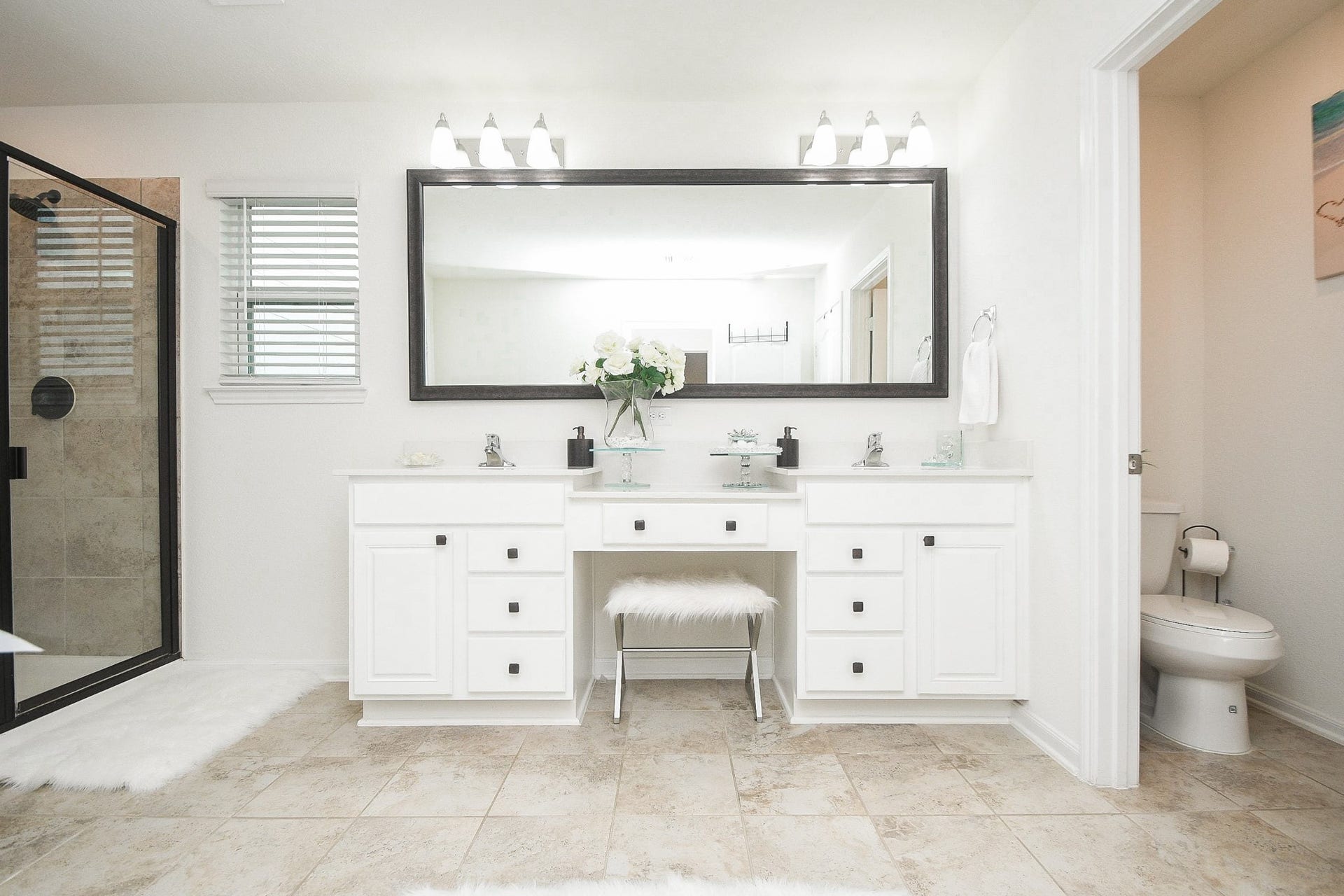 22523 Strathmore Drive, Richmond, TX 77469 This bathroom features a spacious double vanity with sleek white cabinetry and a large framed mirror. It includes a glass-enclosed shower, elegant light fixtures, and neutral tile flooring, creating a bright and modern space.