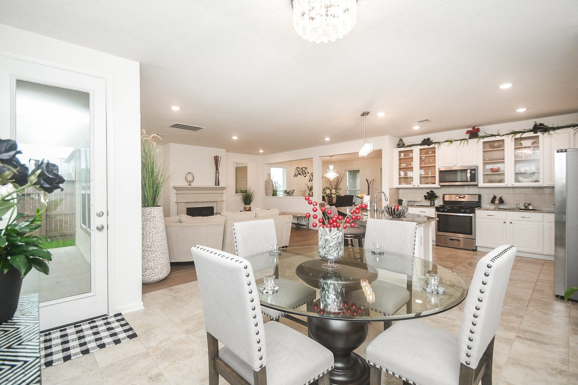 22523 Strathmore Drive, Richmond, TX 77469 Open-concept living space featuring a modern kitchen with stainless steel appliances, a breakfast nook area with a glass table, and a backyard entrance on the left. The space is bright and airy, accented by neutral tones and stylish decor.