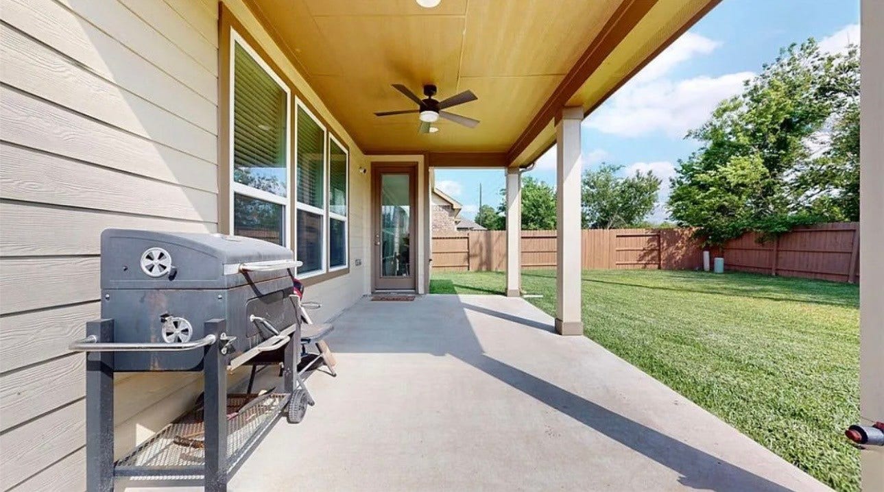 22523 Strathmore Drive, Richmond, TX 77469 This photo showcases a covered patio with a ceiling fan, offering a comfortable outdoor space. It features large windows for natural light and a view of a fenced green yard, ideal for relaxation or entertaining.