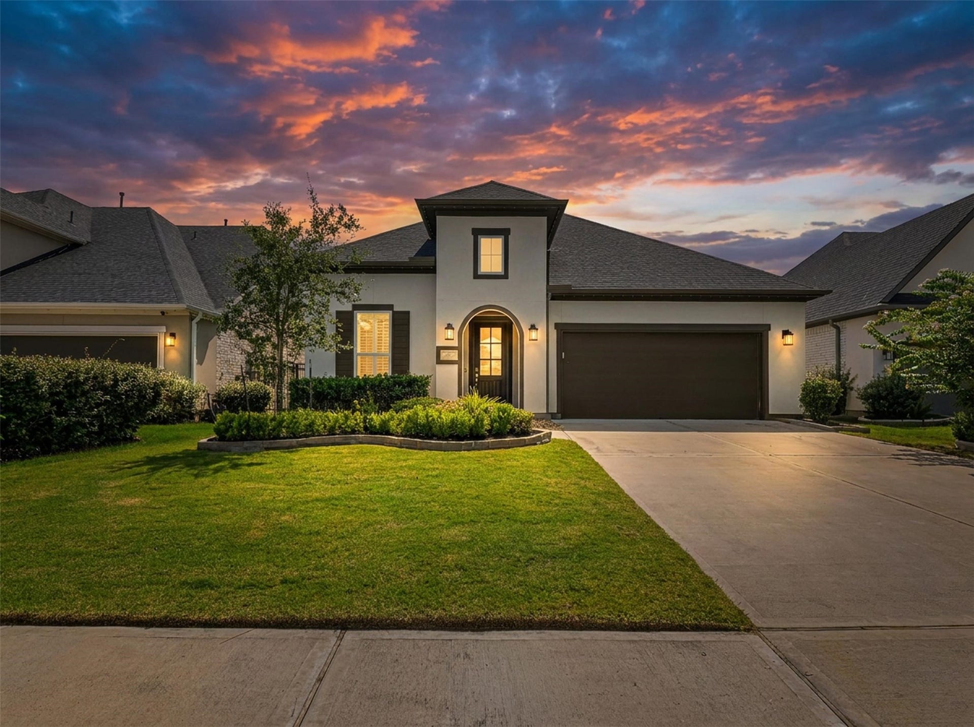 28314 Emerald Bend, Spring, TX 77386 A grand two-story elevation showcases sleek stucco, dark accent shutters, stone-bordered landscaping, and an arched entry under sunset skies. An expansive driveway leads to the attached two-car garage, completing the stunning exterior curb appeal of this Houston home.