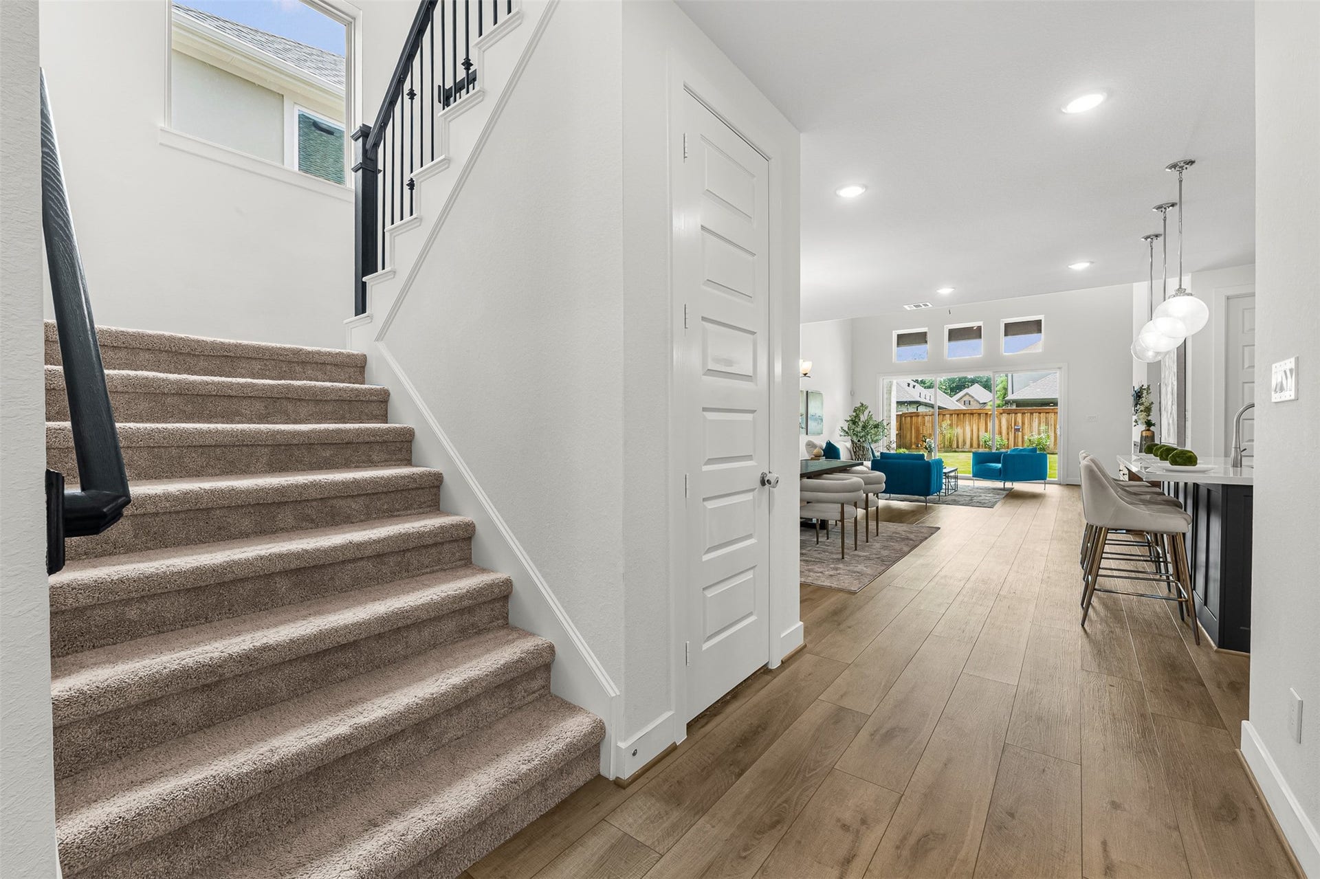 28314 Emerald Bend, Spring, TX 77386 Plank flooring stretches from the entry hallway into the main floor living space, passing a carpeted staircase with wrought-iron balusters. A main-floor storage closet sits near the kitchen island, offering convenient organization steps from the central living area.