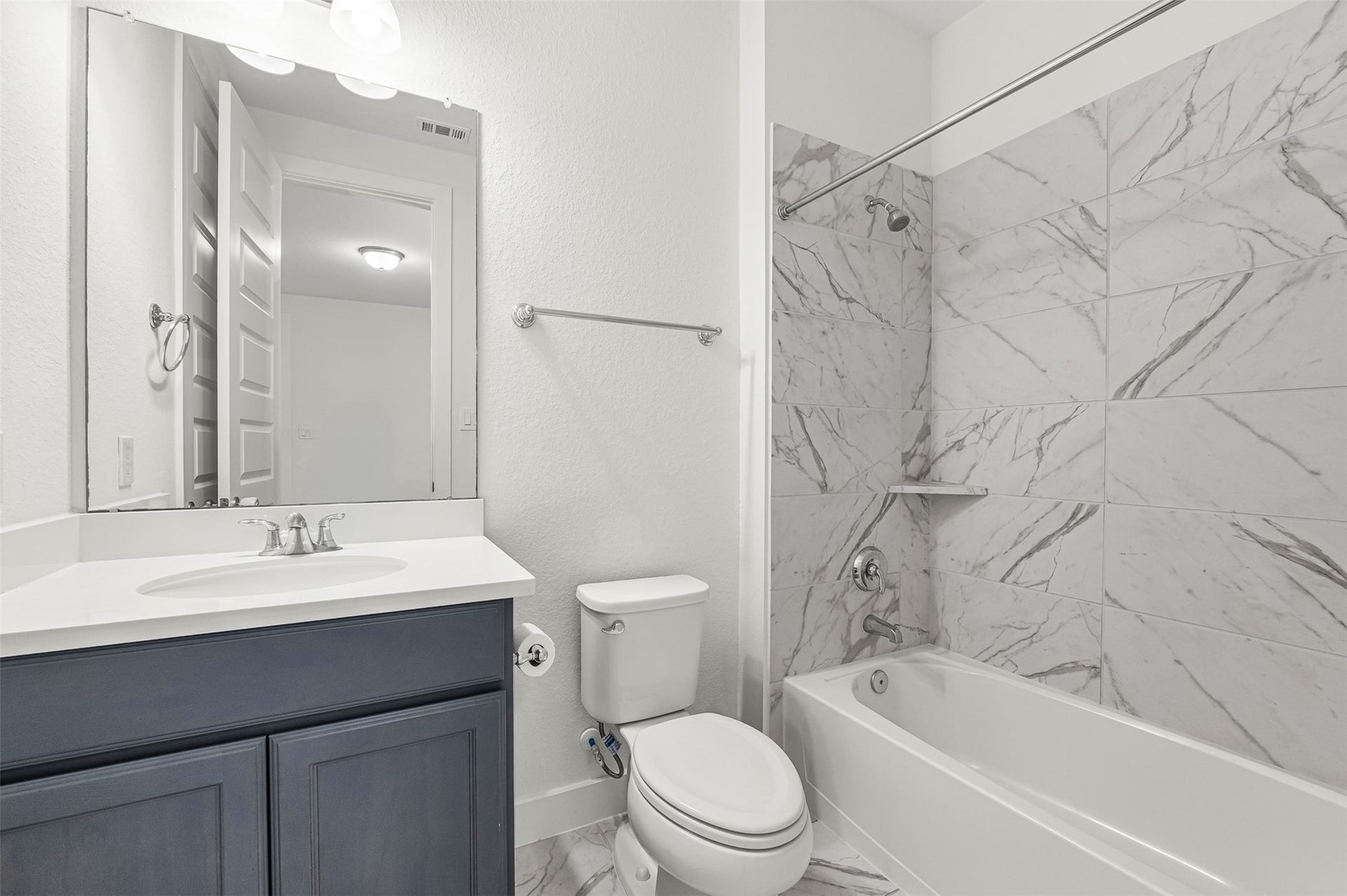 28314 Emerald Bend, Spring, TX 77386 Contemporary navy vanity cabinetry pairs with crisp white quartz countertops and a sleek undersink basin in this full bathroom. Marble-inspired wall tile surrounds the tub-and-shower combination, adding a refined touch to the space.