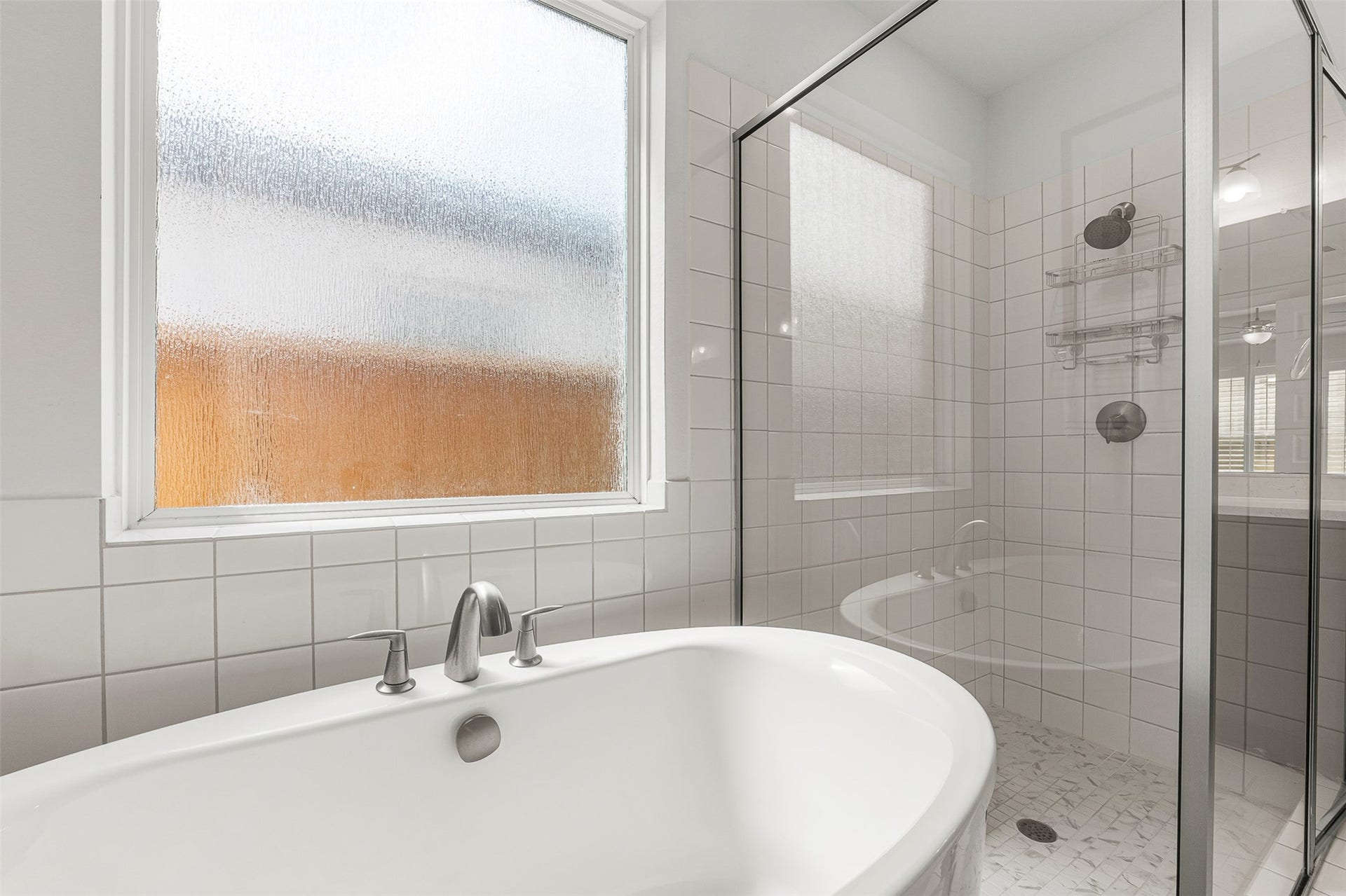 28314 Emerald Bend, Spring, TX 77386 A deep freestanding soaking tub and a sleek glass-enclosed shower with a marble-patterned tile floor create a spa-like retreat in this primary ensuite. Crisp white square wall tiles and textured privacy windows flood the space with soft light while maintaining complete seclusion.