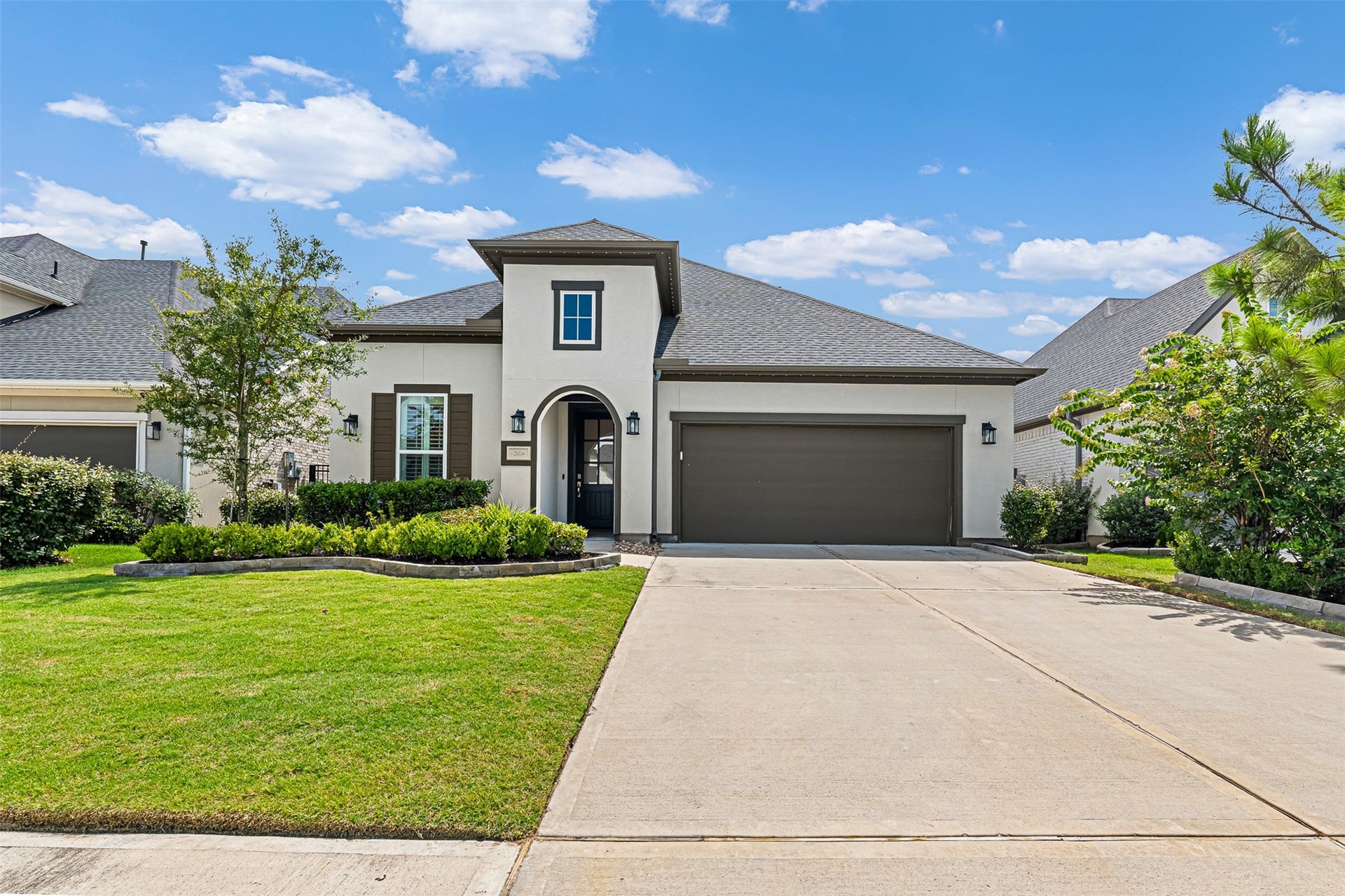 28314 Emerald Bend, Spring, TX 77386 Featuring a sleek stucco finish, dark accent shutters, and an arched entry, this two-story contemporary home makes a striking impression. An expansive concrete driveway leads to the attached two-car garage, framed by manicured green space and stone-bordered landscaping.