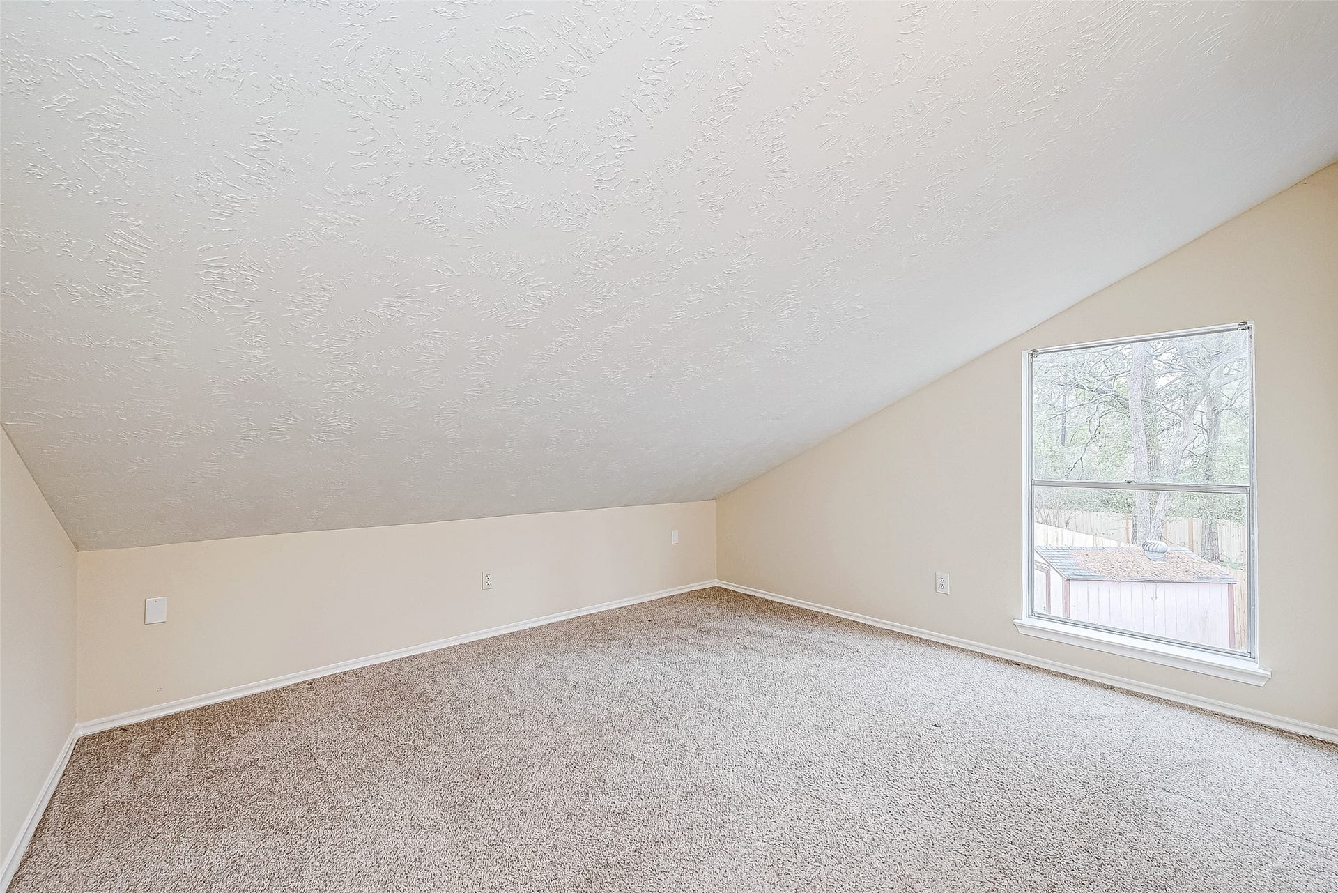 A flexible space with a sloping ceiling and a large window offers endless possibilities. Whether used as a study, playroom, or hobby area, this carpeted room adapts to your needs.