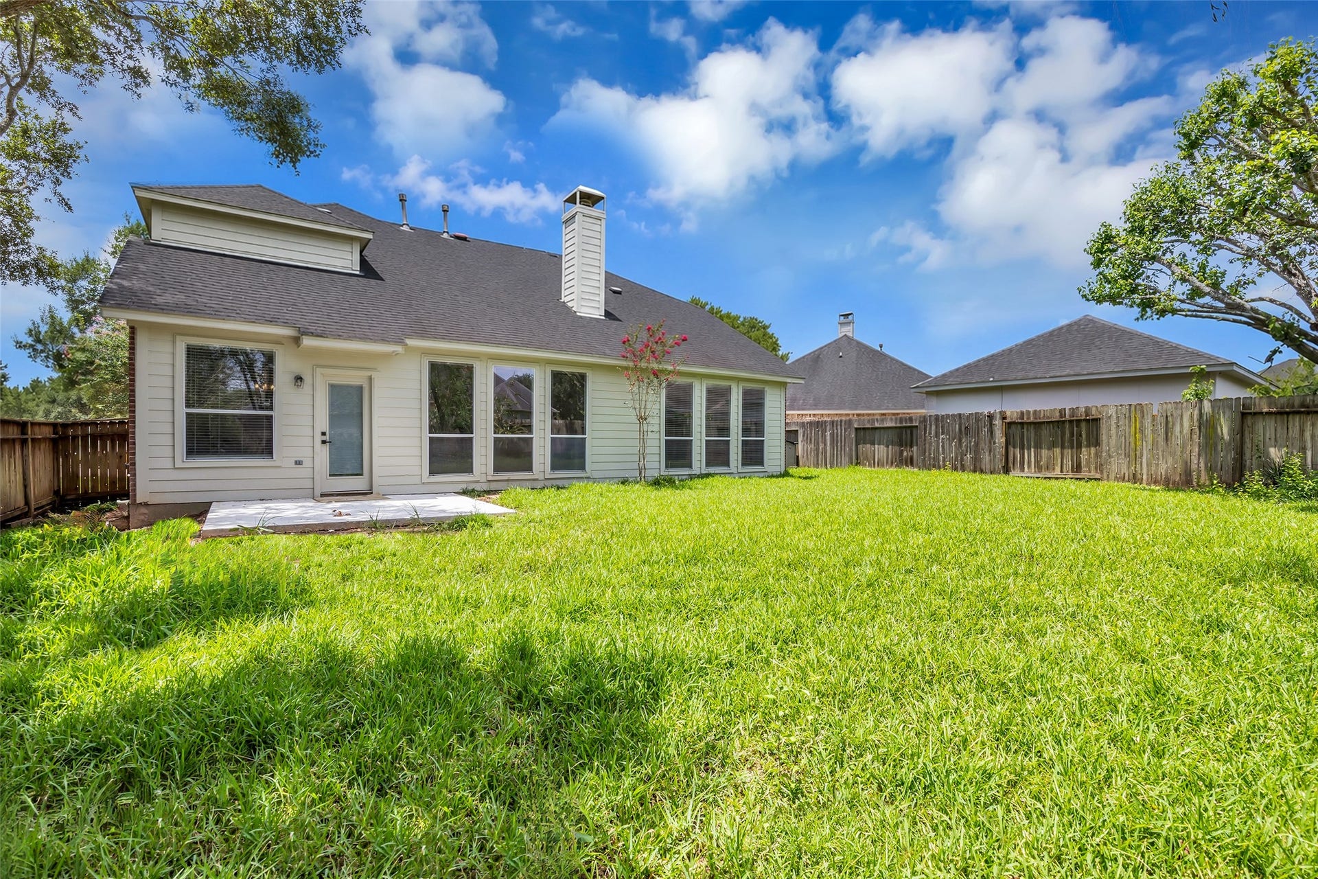 22002 Madera Canyon Court, Richmond, TX 77469 Spacious backyard with a well-maintained lawn, bordered by a wooden fence, and featuring a fresh concrete patio area perfect for outdoor gatherings. The house boasts a modern exterior with large windows offering abundant natural light.