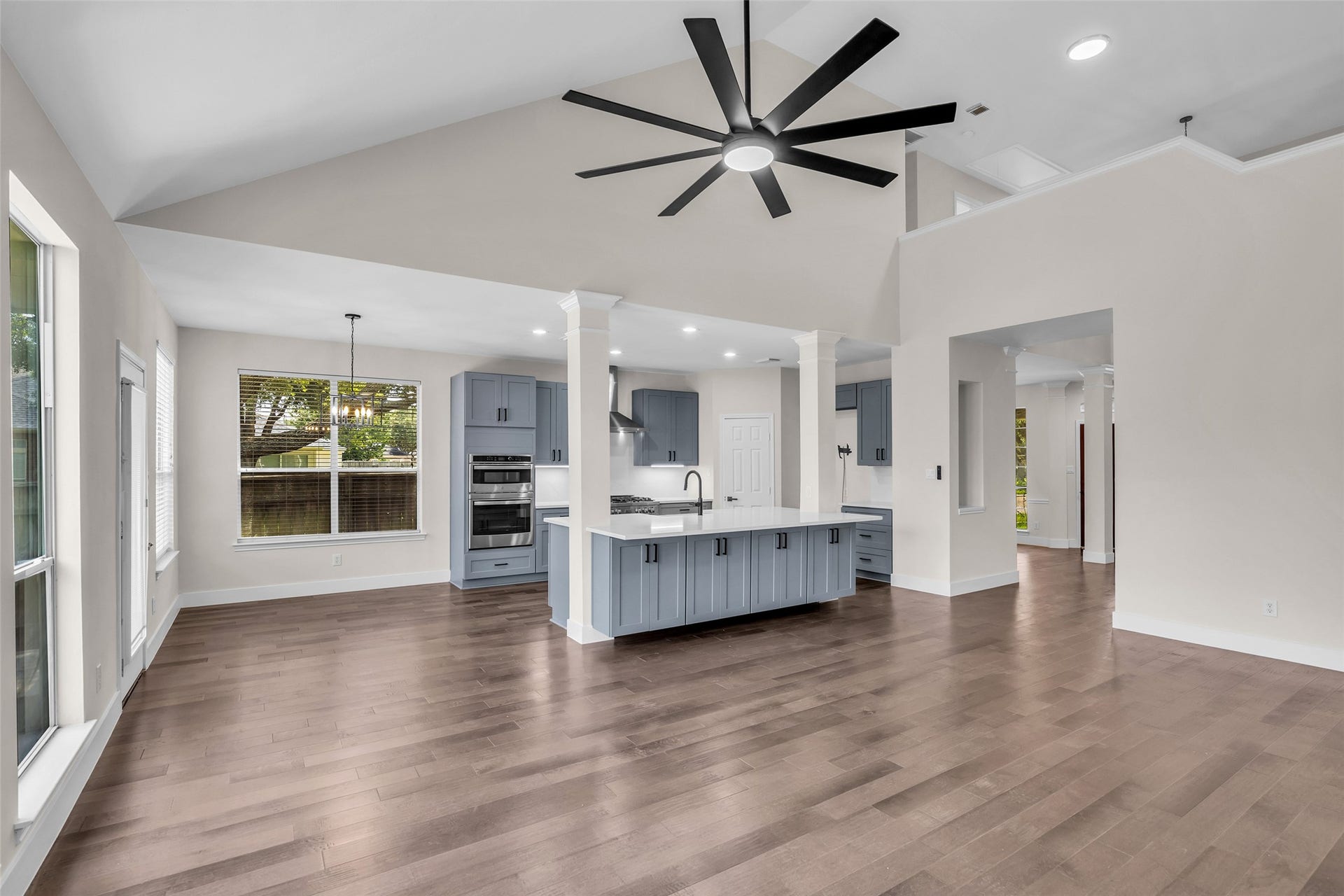22002 Madera Canyon Court, Richmond, TX 77469 Spacious and modern open-concept kitchen with sleek gray cabinetry, a large island, and elegant hardwood floors, enhanced by abundant natural light and a striking ceiling fan.