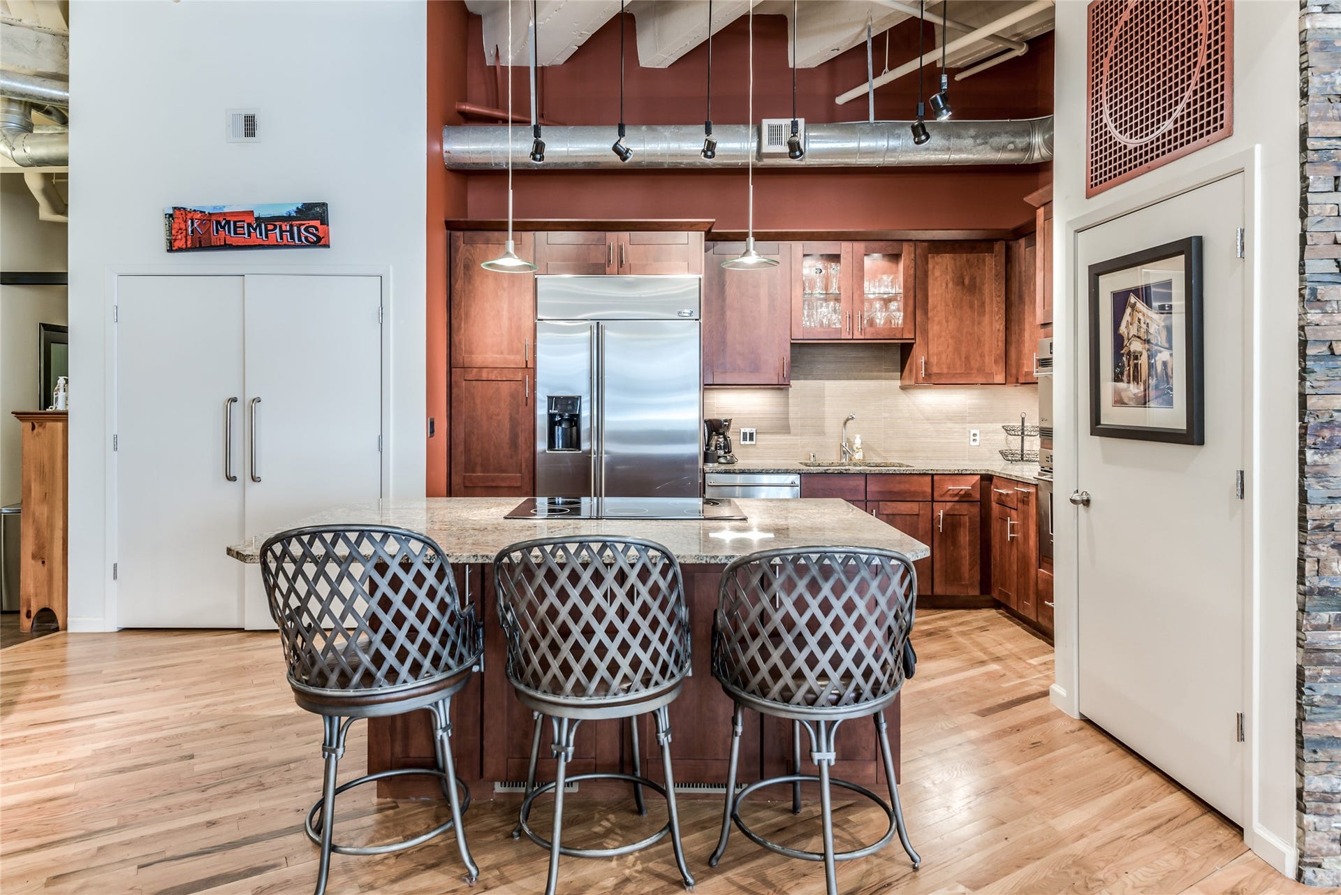 705 Main Street, #215, Houston, TX 77002 This kitchen features a modern industrial design with exposed ductwork and high ceilings. It includes a spacious island with granite countertops and seating.