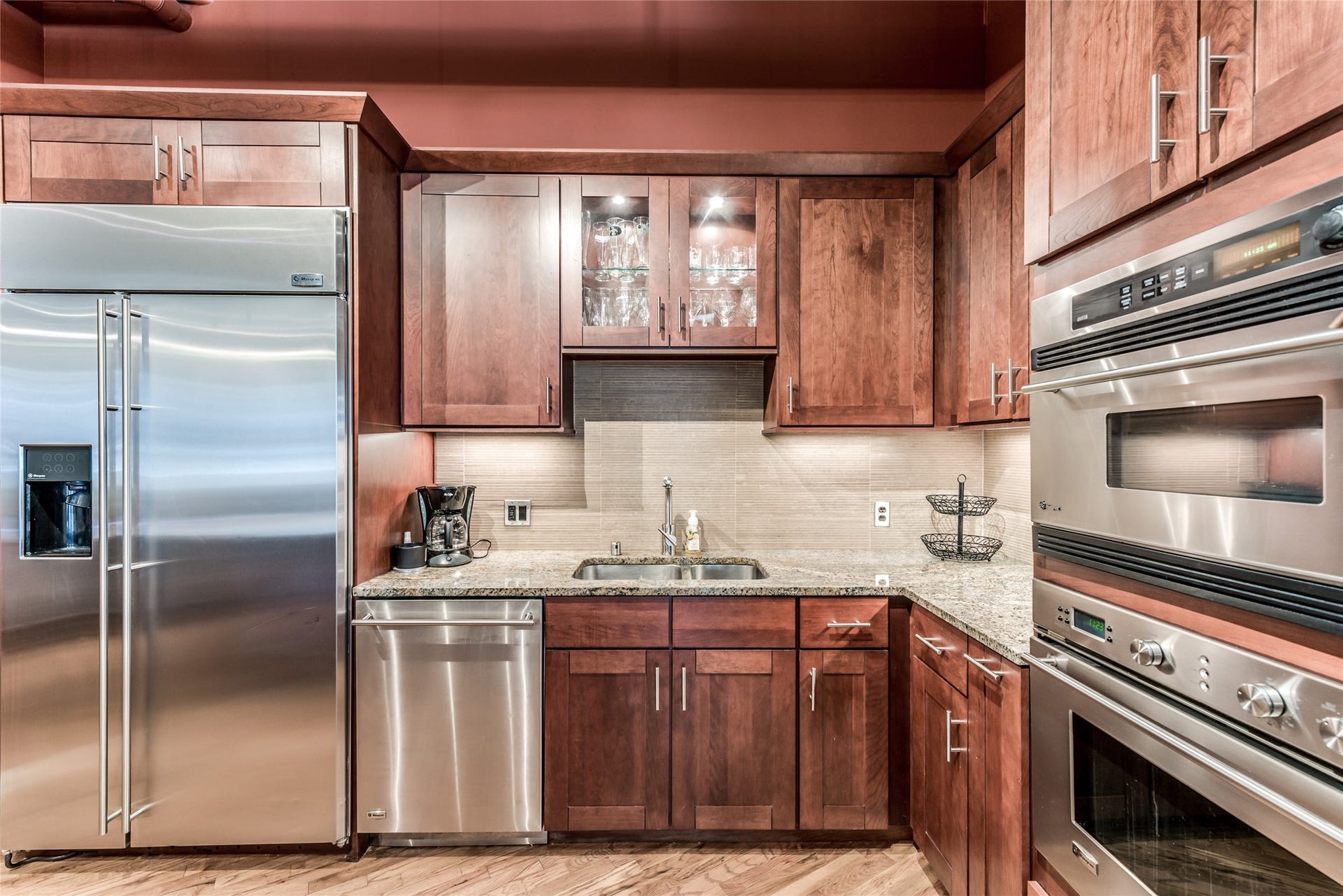705 Main Street, #215, Houston, TX 77002 This kitchen features modern stainless steel appliances, including a double oven and a large fridge. It has rich wooden cabinetry, granite countertops, and a stylish tile backsplash, offering both functionality and elegance.