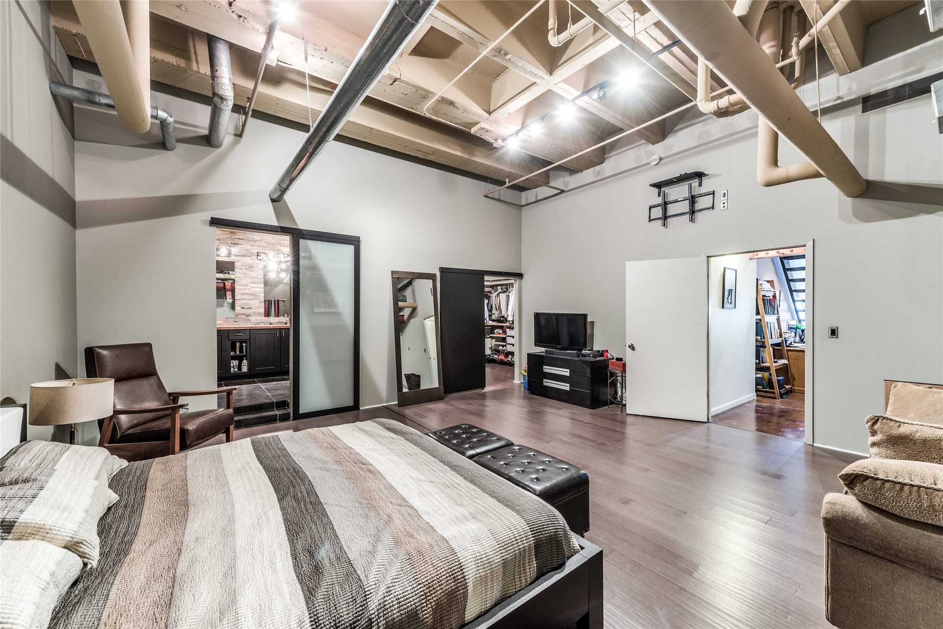 705 Main Street, #215, Houston, TX 77002 This spacious, industrial-style primary bedroom features high ceilings with exposed ductwork, modern lighting, and wood flooring.