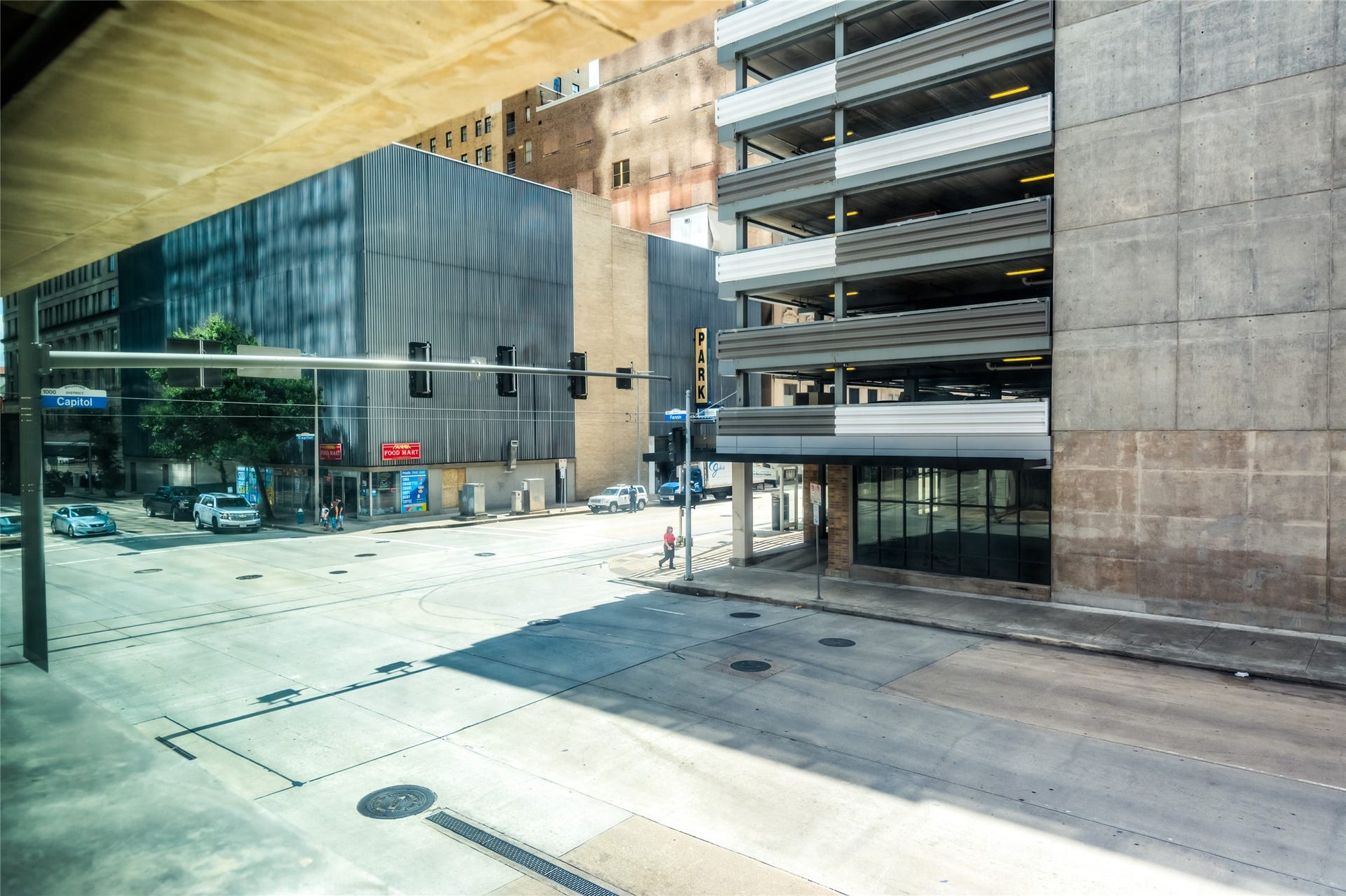 705 Main Street, #215, Houston, TX 77002 Urban view featuring a street corner with a parking garage and modern commercial buildings. Wide sidewalks and minimal traffic provide a spacious city feel.