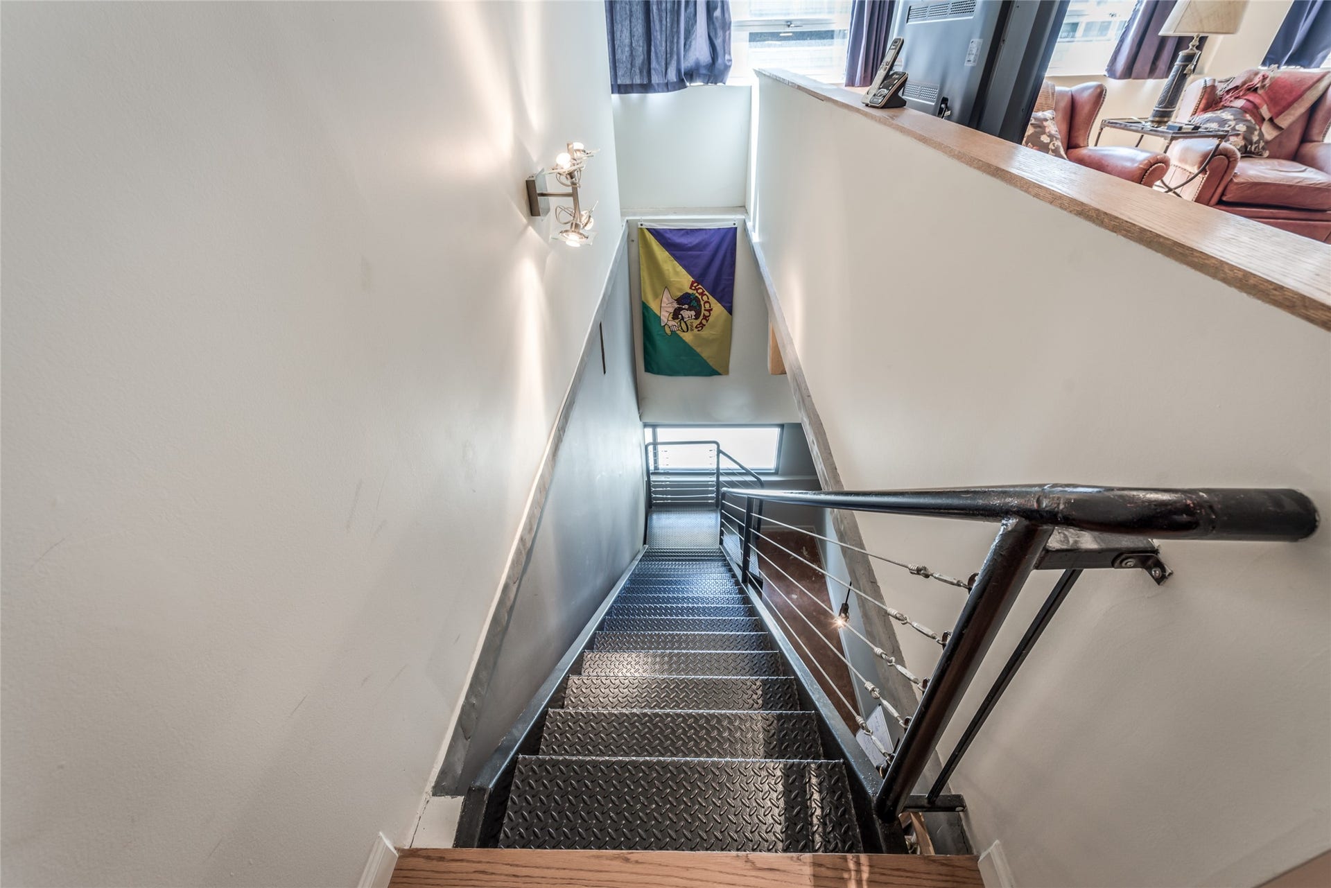 705 Main Street, #215, Houston, TX 77002 This photo showcases a modern staircase with metal steps and a sleek railing, leading to lower level area to primary bedroom with natural light from large windows.