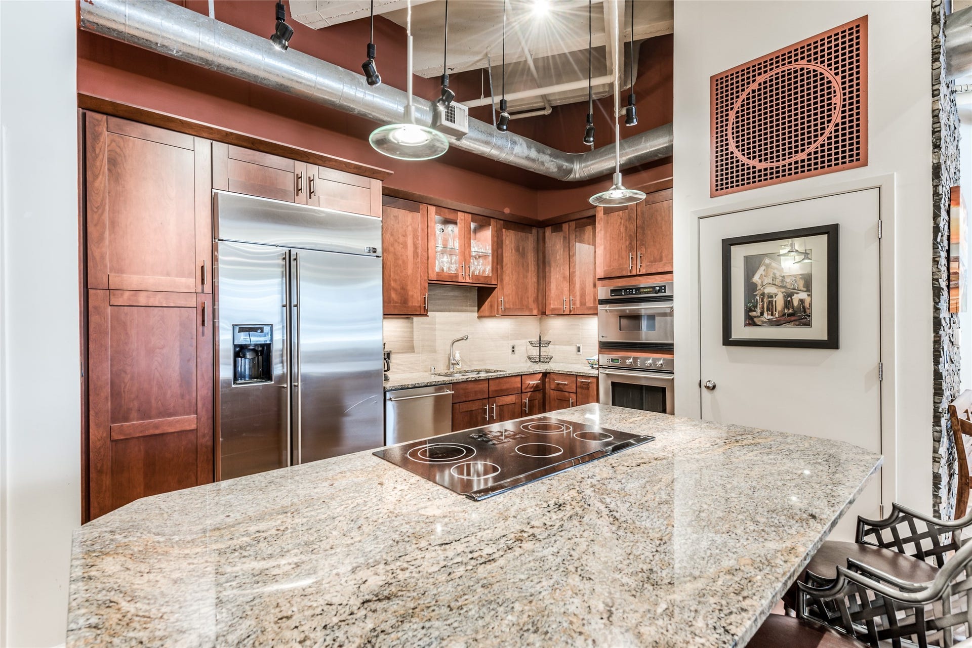 705 Main Street, #215, Houston, TX 77002 Modern kitchen with stainless steel appliances, granite countertops, and rich wooden cabinetry. Features an island with a built-in cooktop and industrial-style lighting, offering a stylish and functional space.