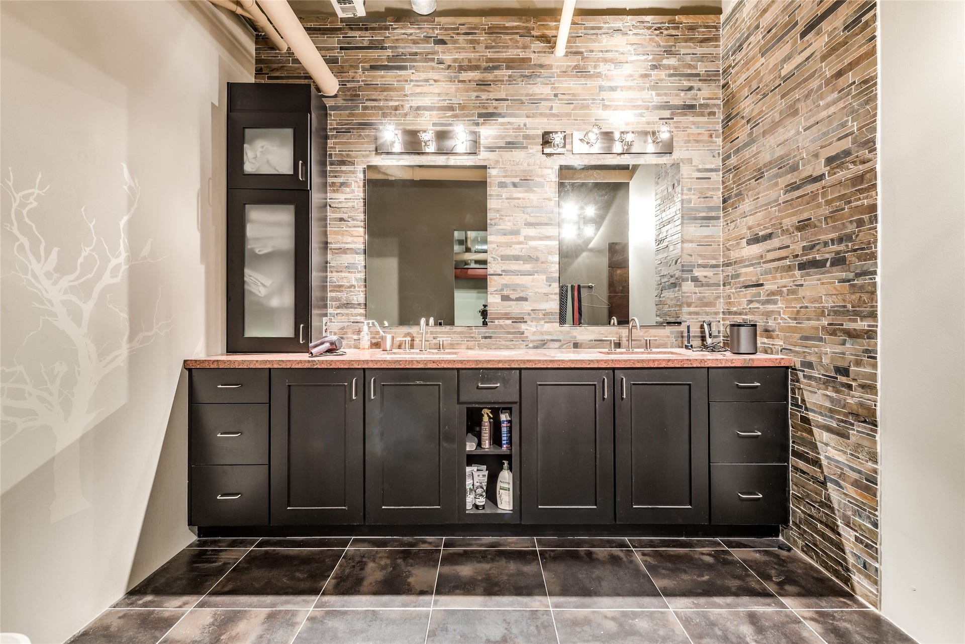 705 Main Street, #215, Houston, TX 77002 This modern primary bathroom features a double vanity with dark cabinetry and a sleek stone-tiled wall.