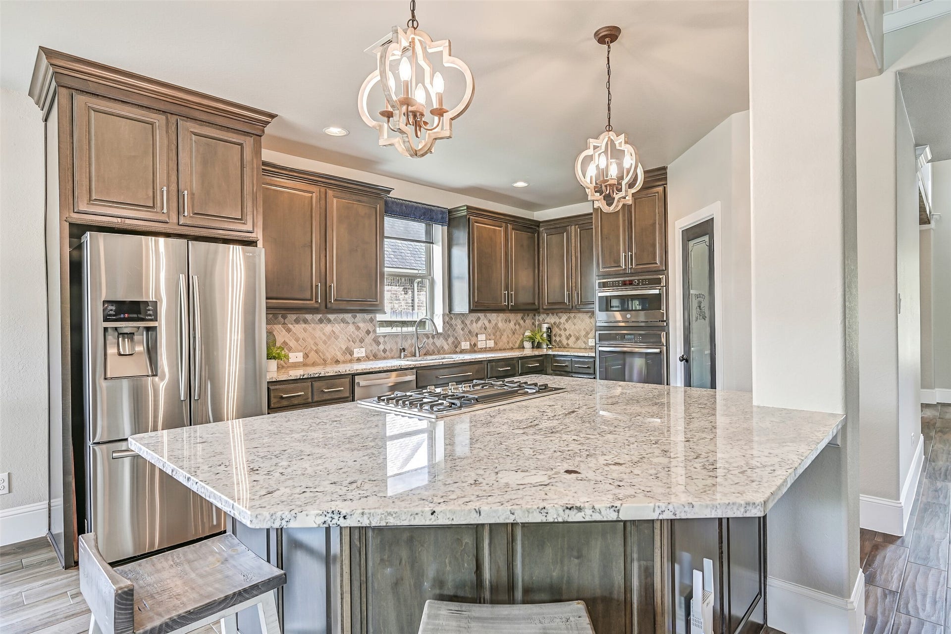 An expansive granite island provides impressive prep space and seating while housing the 4-burner downdraft cooktop. Abundant cabinetry, recessed lighting and decorative pendants complete this well-appointed kitchen.