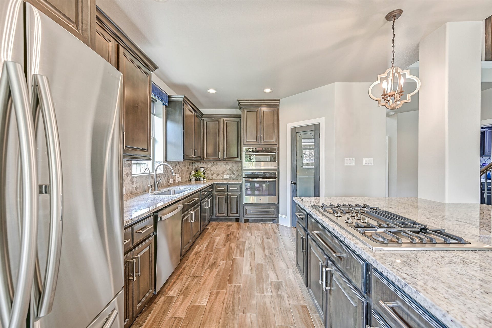 Designed with plenty of workspace and storage, the kitchen features granite counters, stained wood cabinetry, arabesque tile backsplash & stainless appliances, plus a corner pantry with glass door and custom pull-out storage.