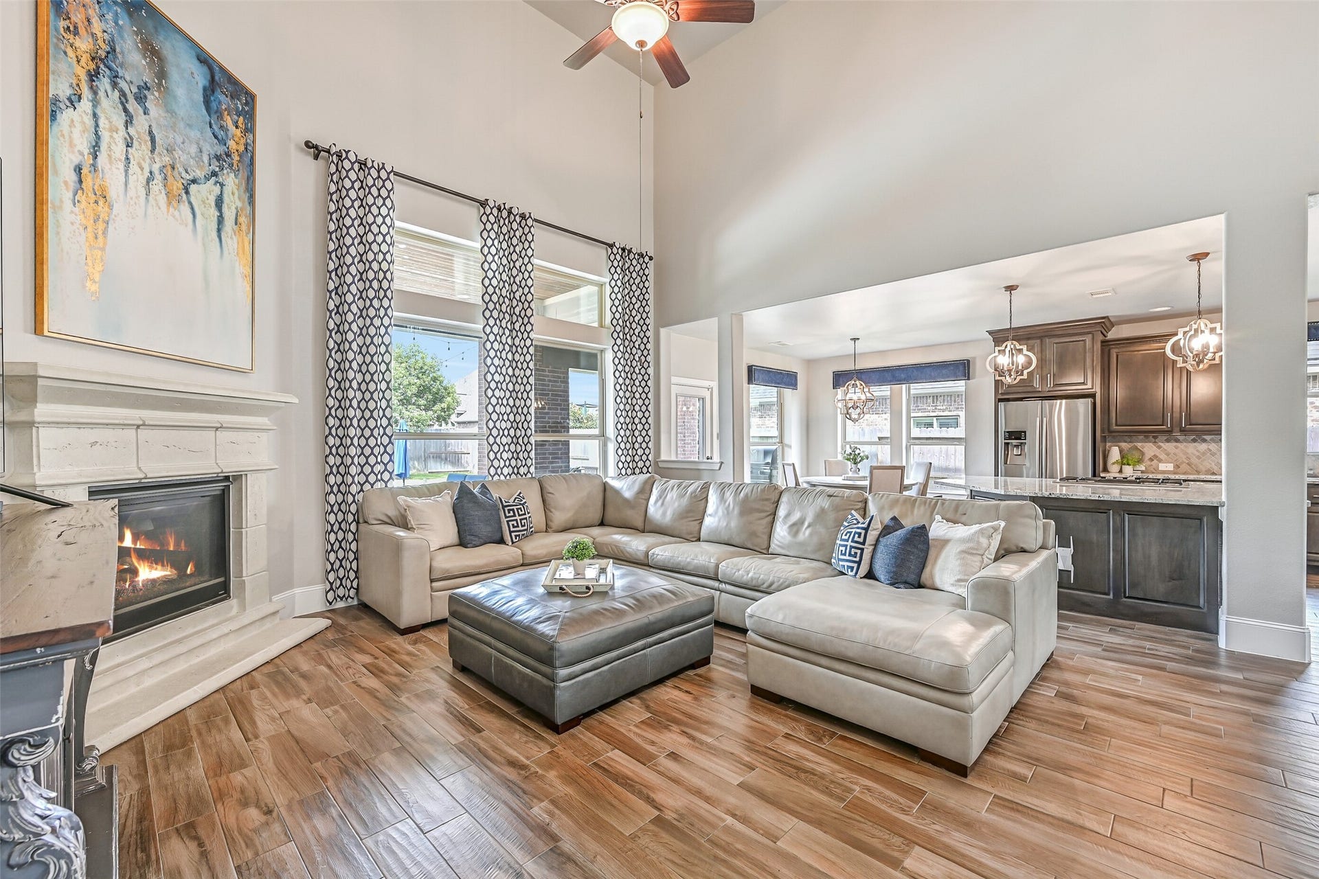 Soaring 19' ceilings make an impressive statement in the spacious family room, where a cast-stone gas-log fireplace, wall of pool-view windows & wood-look tile floors complement the open flow into the island kitchen and breakfast room.