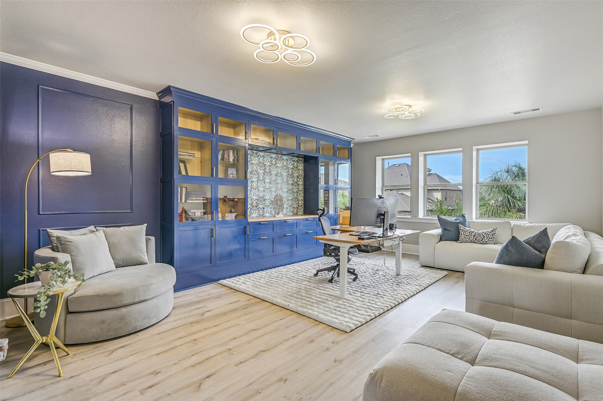 The spacious second-floor gameroom offers LVP flooring, modern lighting, a wall of rear-facing windows with pool views and an impressive custom built-in with glass-front cabinetry, display shelving and abundant storage.