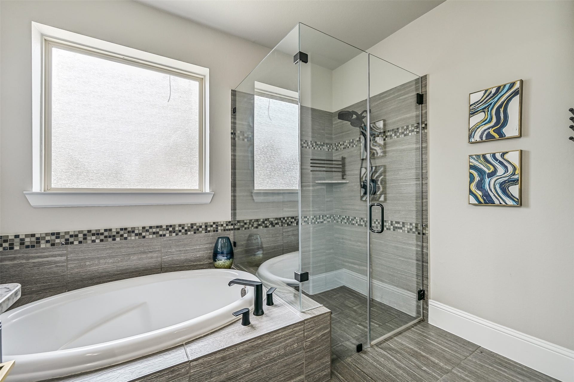 The spacious seamless-glass shower features dual showerheads and tiled surround, complemented by a separate soaking tub and coordinating tilework for a relaxing, spa-inspired retreat.