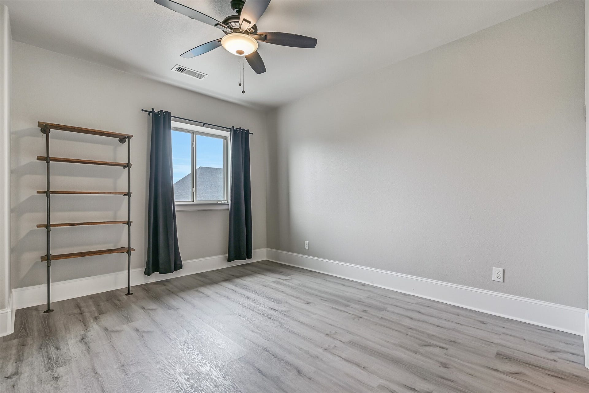 Another generously sized upstairs bedroom offers neutral paint, LVP flooring, a lighted ceiling fan and industrial-style wall shelving, with convenient access to the adjoining Jack & Jill-style bath.