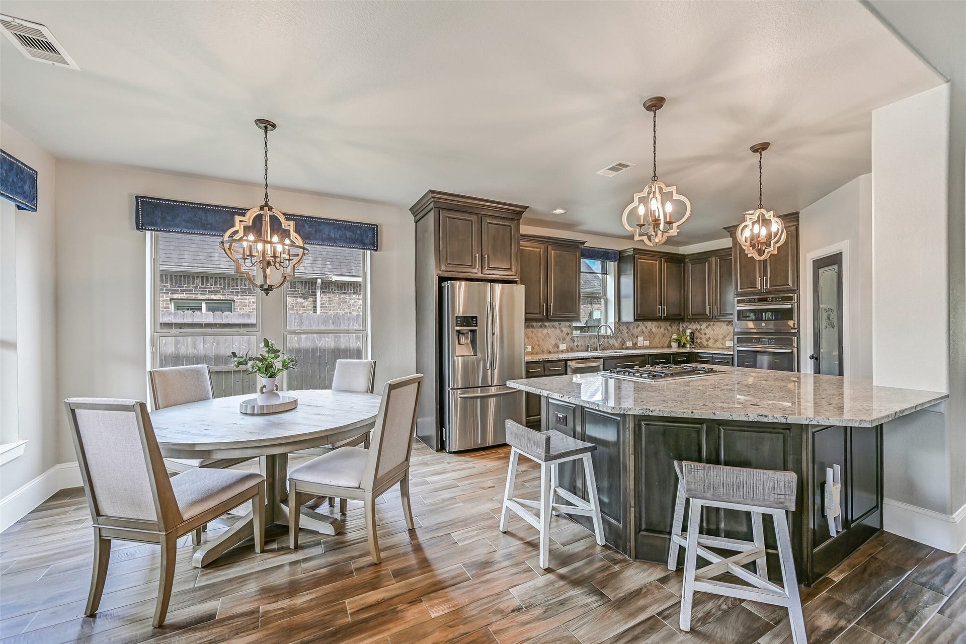 The open kitchen centers around an oversized granite island with generous seating, surrounded by stained wood cabinetry, stainless appliances and updated lighting, with the adjoining breakfast room just steps away.