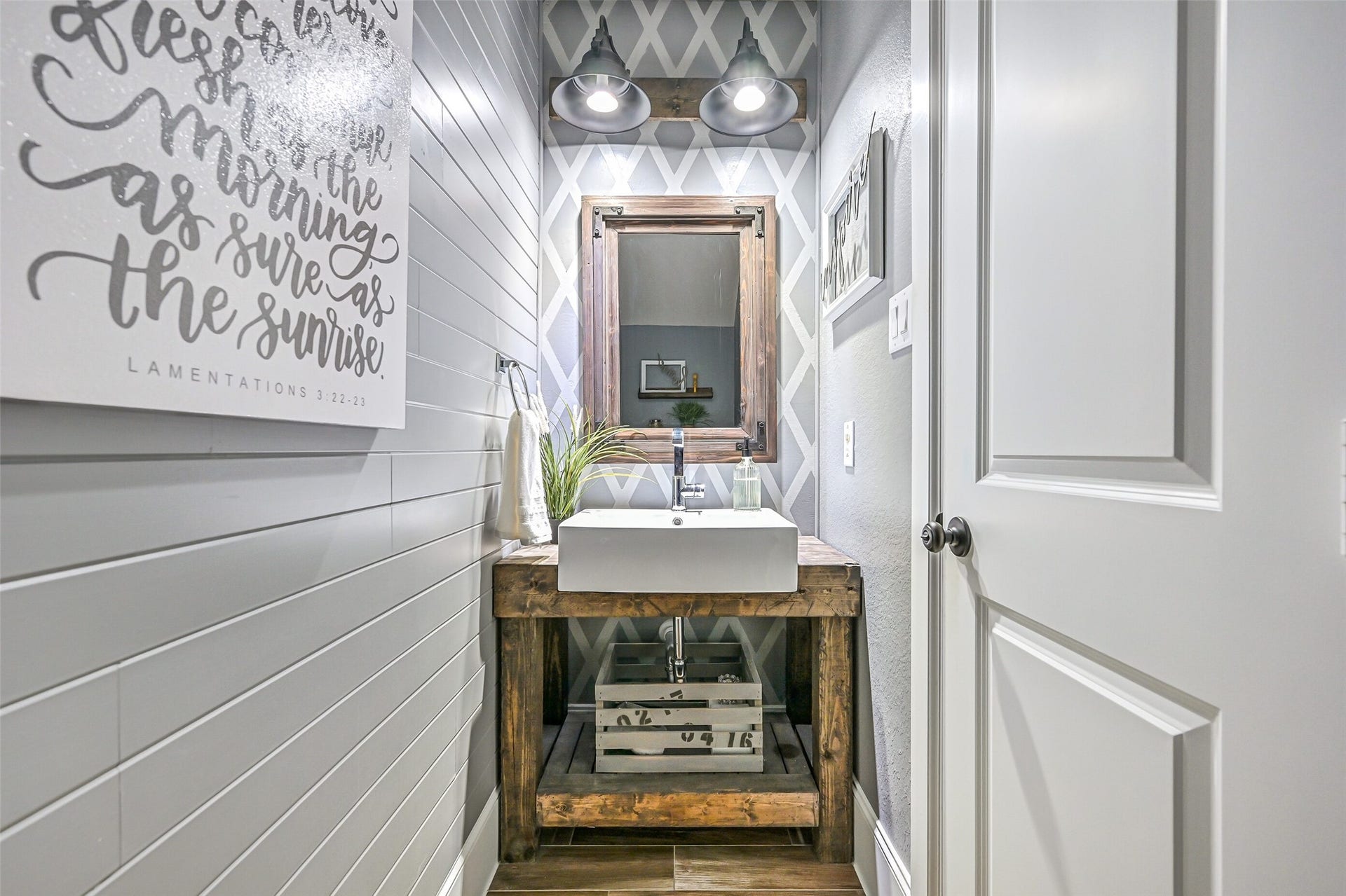 Tucked into a convenient alcove off the family room, this stylish powder bath features shiplap, a geometric accent wall, rustic wood vanity with vessel sink, industrial-style lighting & coordinating framed mirror.
