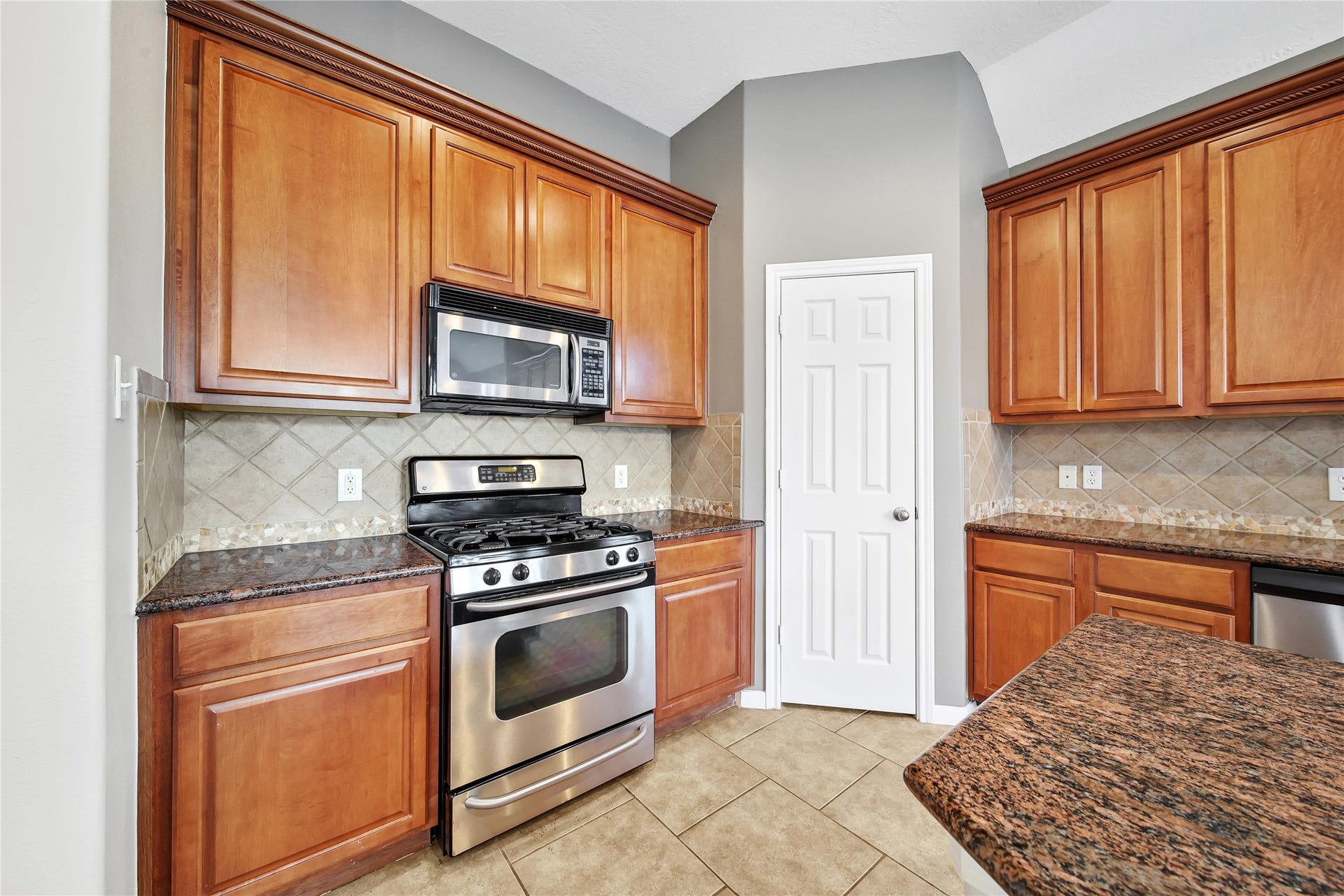 25604 Southwood Oaks Court, Porter, TX 77365 This kitchen features warm-toned wooden cabinetry, granite countertops, stainless steel appliances, a built-in microwave, and a gas stove. It has tiled backsplash and flooring, with a neutral color scheme.