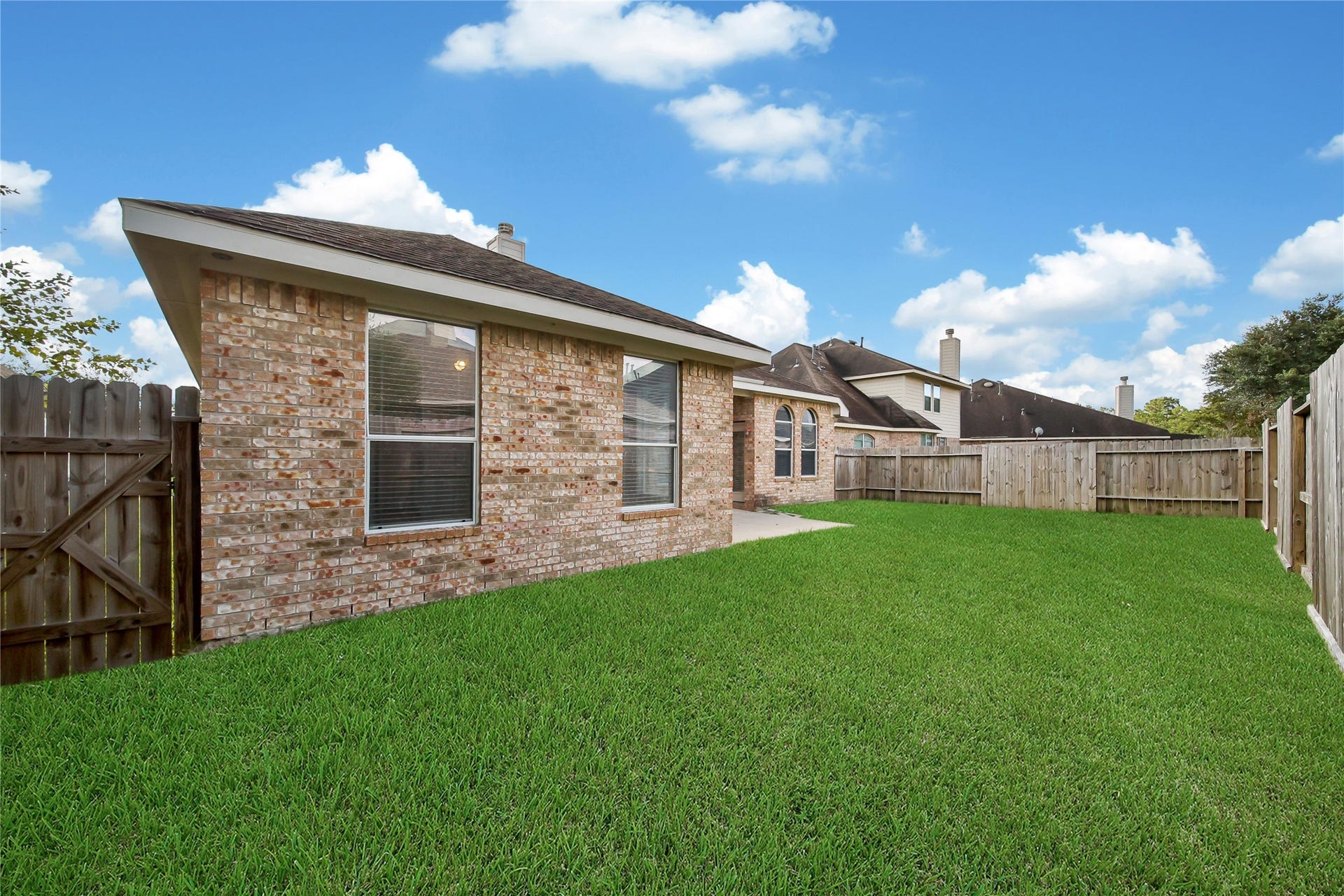 25604 Southwood Oaks Court, Porter, TX 77365 This is a single-story brick home with a back lawn and a privacy fence, featuring a spacious backyard and a clear sky above.