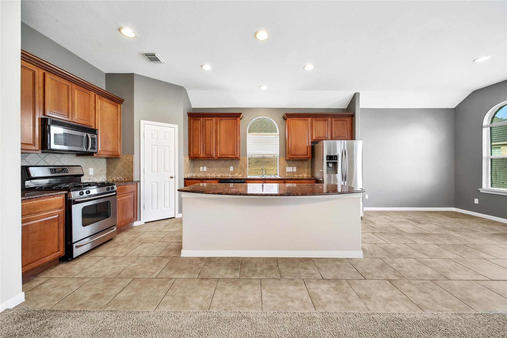 25604 Southwood Oaks Court, Porter, TX 77365 This is a spacious kitchen featuring stainless steel appliances, ample wooden cabinetry, a central island with a countertop, and a mix of tile and carpeted flooring. The area is well-lit with natural light from large windows and has recessed ceiling lights.