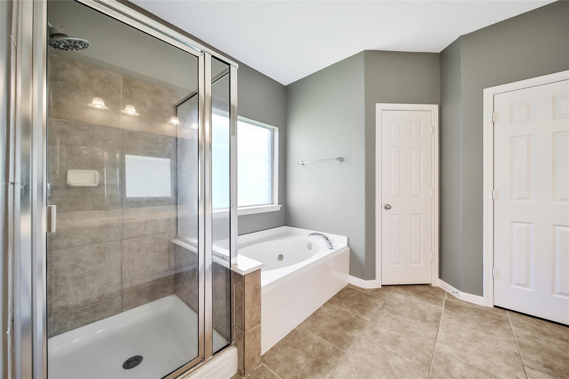 25604 Southwood Oaks Court, Porter, TX 77365 The modern looking primary bathroom features an oversized glass-enclosed shower, a separate bathtub, tiled flooring, and neutral wall colors. It includes a window for natural light, and a huge closet.