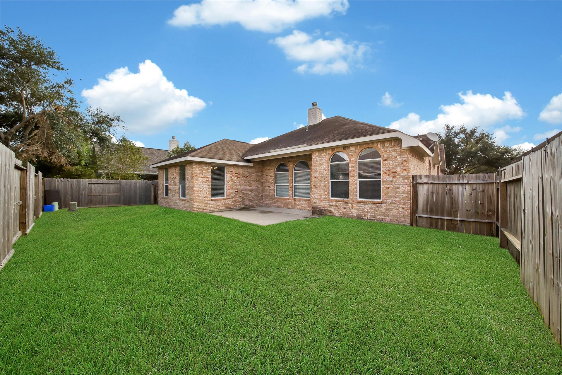 25604 Southwood Oaks Court, Porter, TX 77365 This image showcases a single-story brick home featuring a lawn and a fenced backyard, with ample outdoor space for activities and relaxation. The house has large windows for natural lighting and a concrete patio area.
