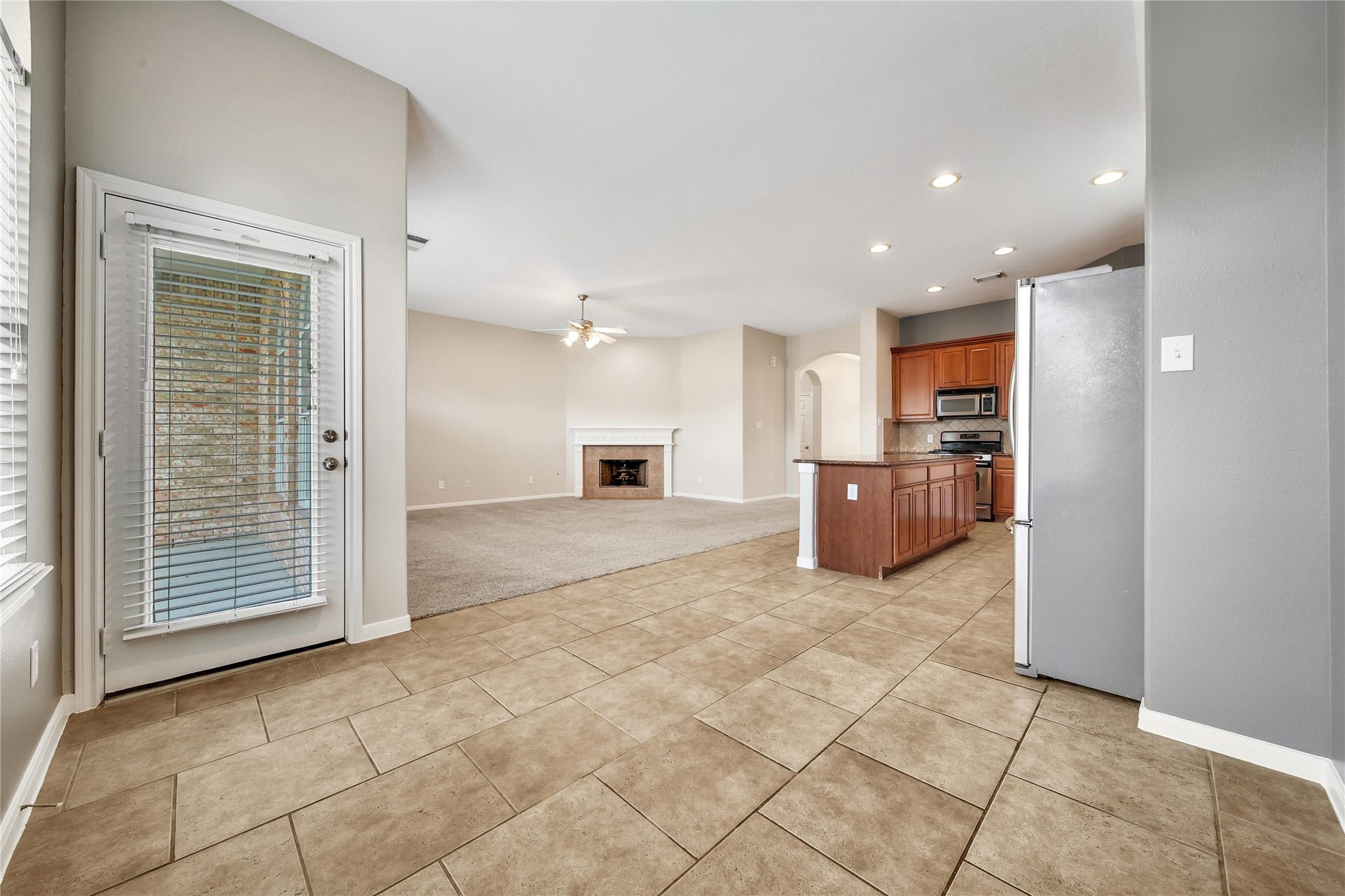 25604 Southwood Oaks Court, Porter, TX 77365 This is a spacious, open-concept living area with tile flooring, leading into a carpeted section with a cozy fireplace. The adjoining kitchen features wooden cabinets and modern appliances, with natural light streaming in from the glass door located off the breakfast room.