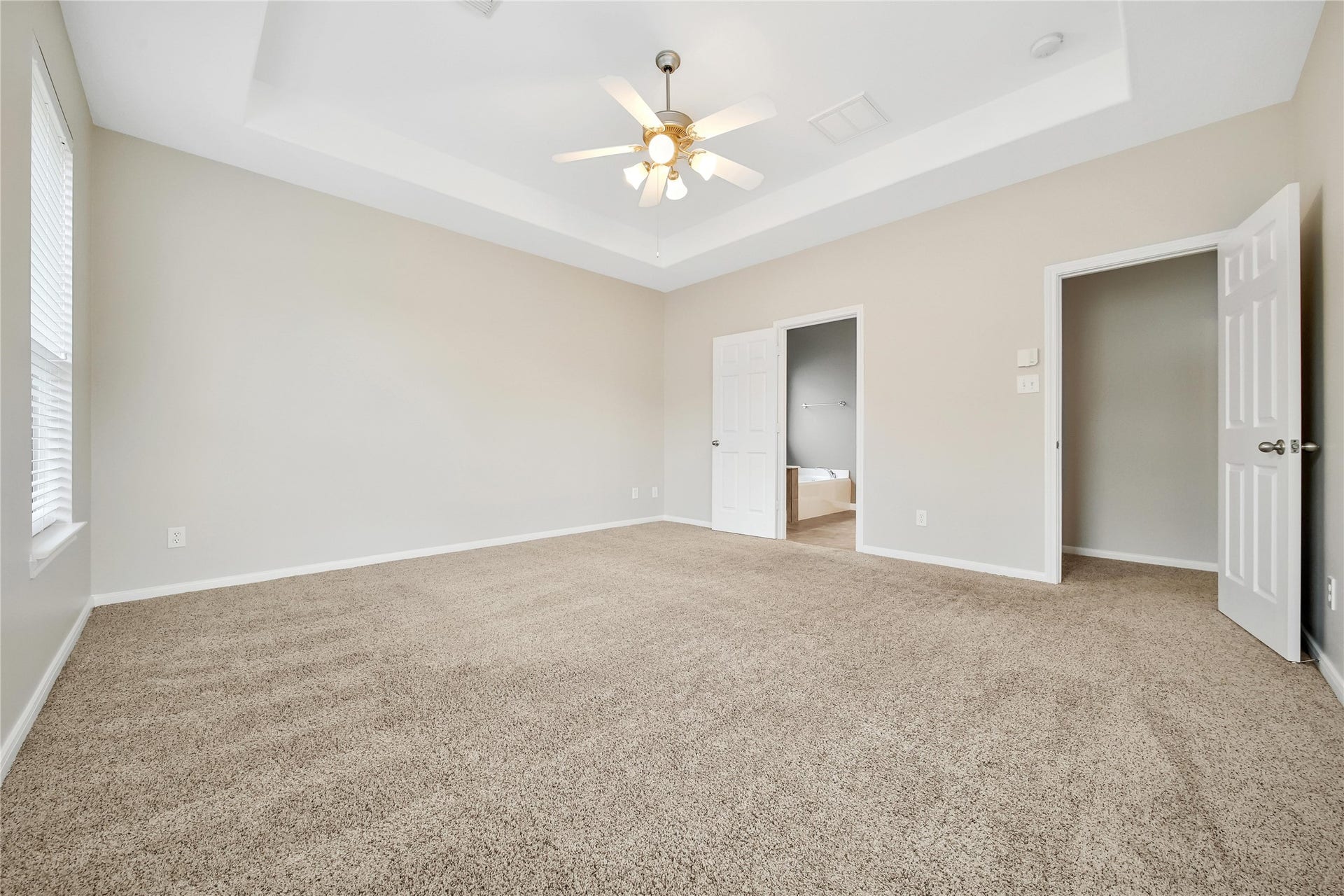25604 Southwood Oaks Court, Porter, TX 77365 This is a spacious, well-lit room Primary Bedroom with neutral walls and carpet flooring, featuring a tray ceiling with a ceiling fan and double doors leading to the well appointed primary bath.