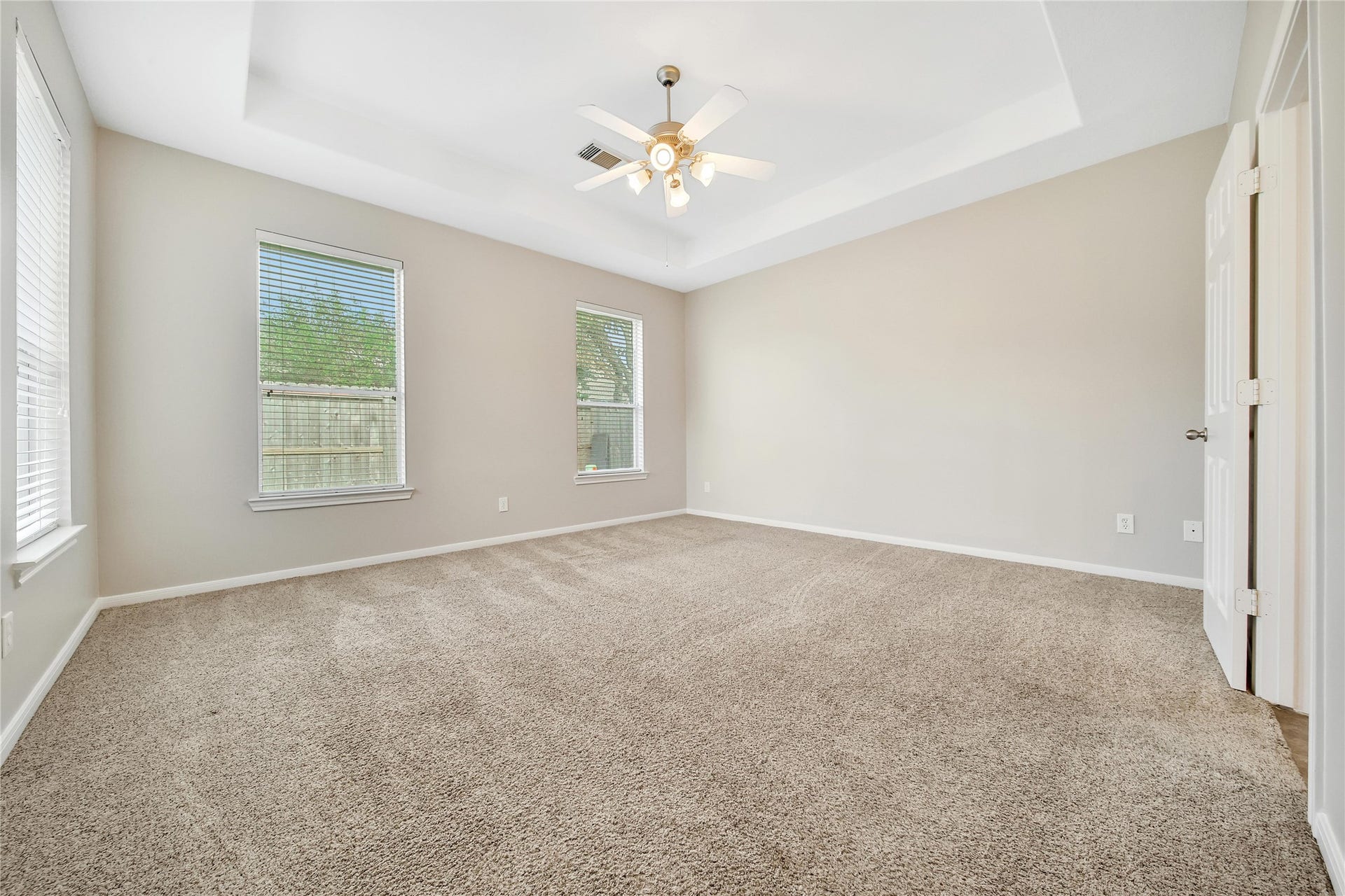 25604 Southwood Oaks Court, Porter, TX 77365 This is a spacious, well-lit Primary Bedroom with neutral walls, carpeting, and a ceiling fan with lighting. It features two large windows that allow for ample natural light.