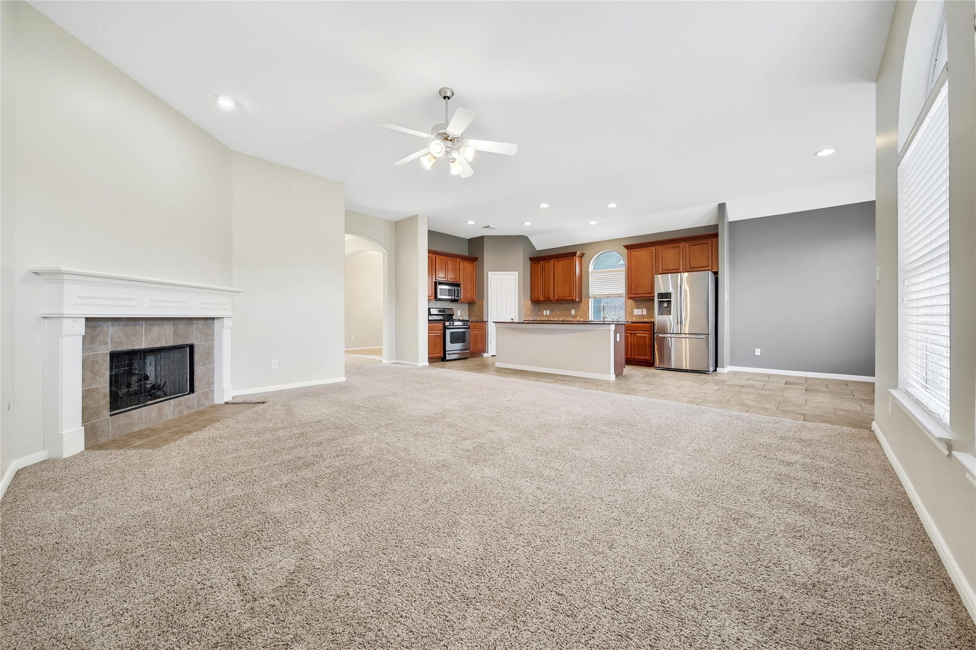 25604 Southwood Oaks Court, Porter, TX 77365 This is a spacious, open-concept living room with plush carpeting, featuring a cozy fireplace and a seamless transition to a tiled kitchen area with wood cabinets and stainless steel appliances. The room is well-lit with natural light from large windows.