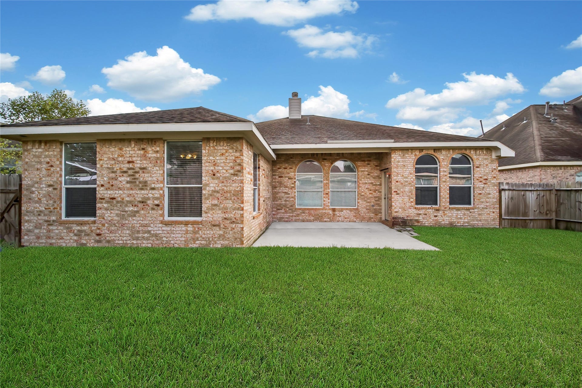 25604 Southwood Oaks Court, Porter, TX 77365 This is a single-story brick home featuring a back lawn and a concrete patio area in the backyard, with a privacy fence surrounding the property.