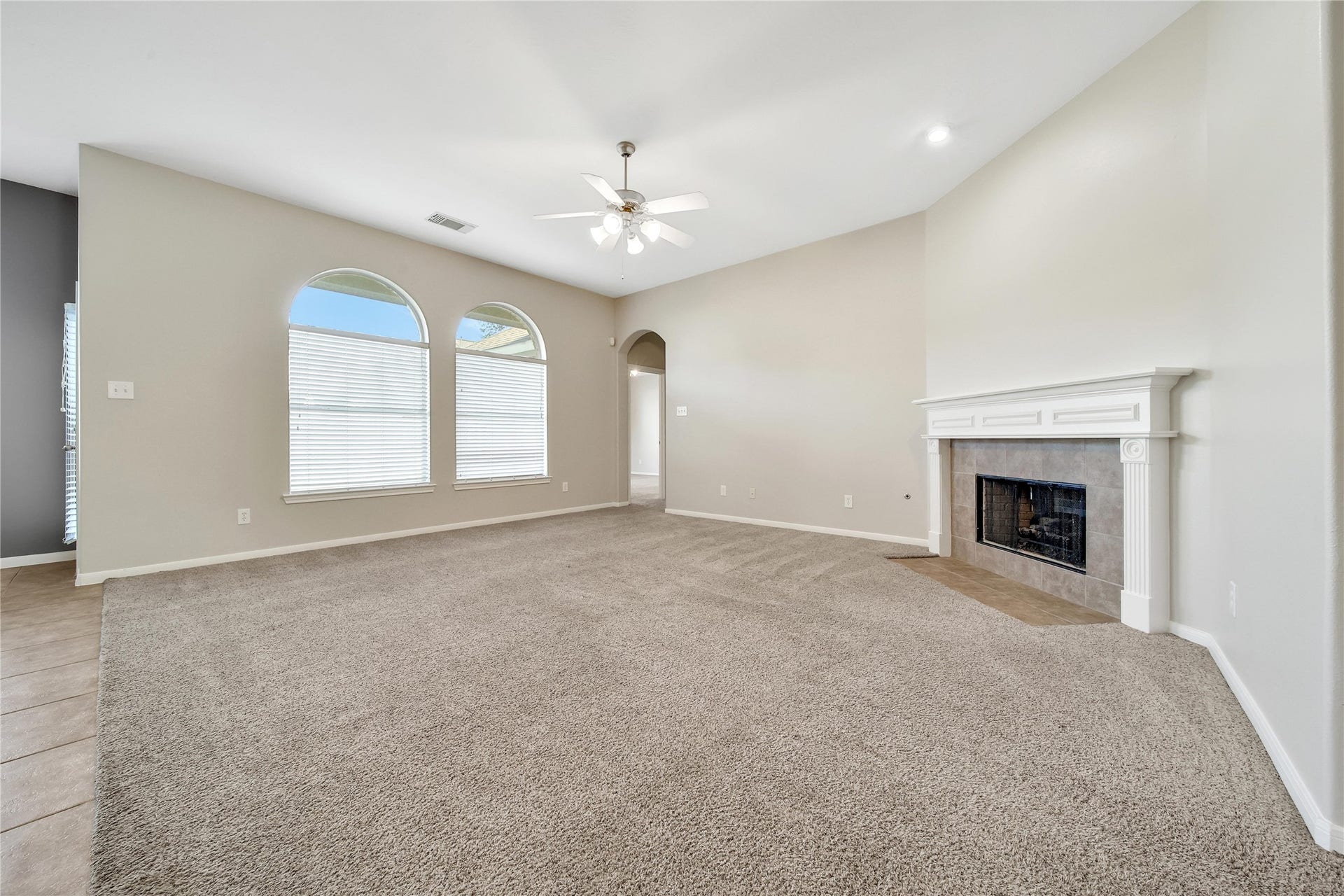 25604 Southwood Oaks Court, Porter, TX 77365 This spacious living room features plush carpeting, large arched windows for ample natural light, a ceiling fan, and an elegant fireplace as the focal point. Alcove of living room leads to primary bedroom.
