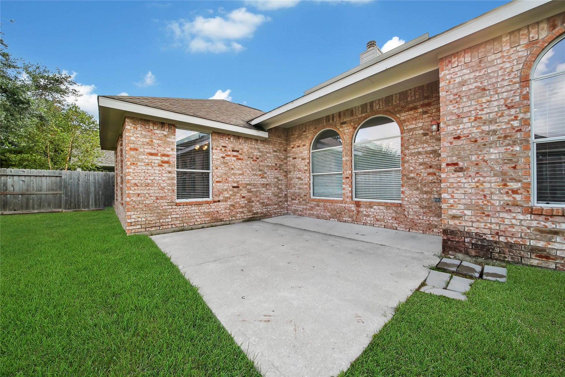25604 Southwood Oaks Court, Porter, TX 77365 This is a well-maintained backyard with a spacious concrete patio and lawn, edged by a tall privacy fence. The exterior features a clean, classic brick finish with several windows allowing for natural light.