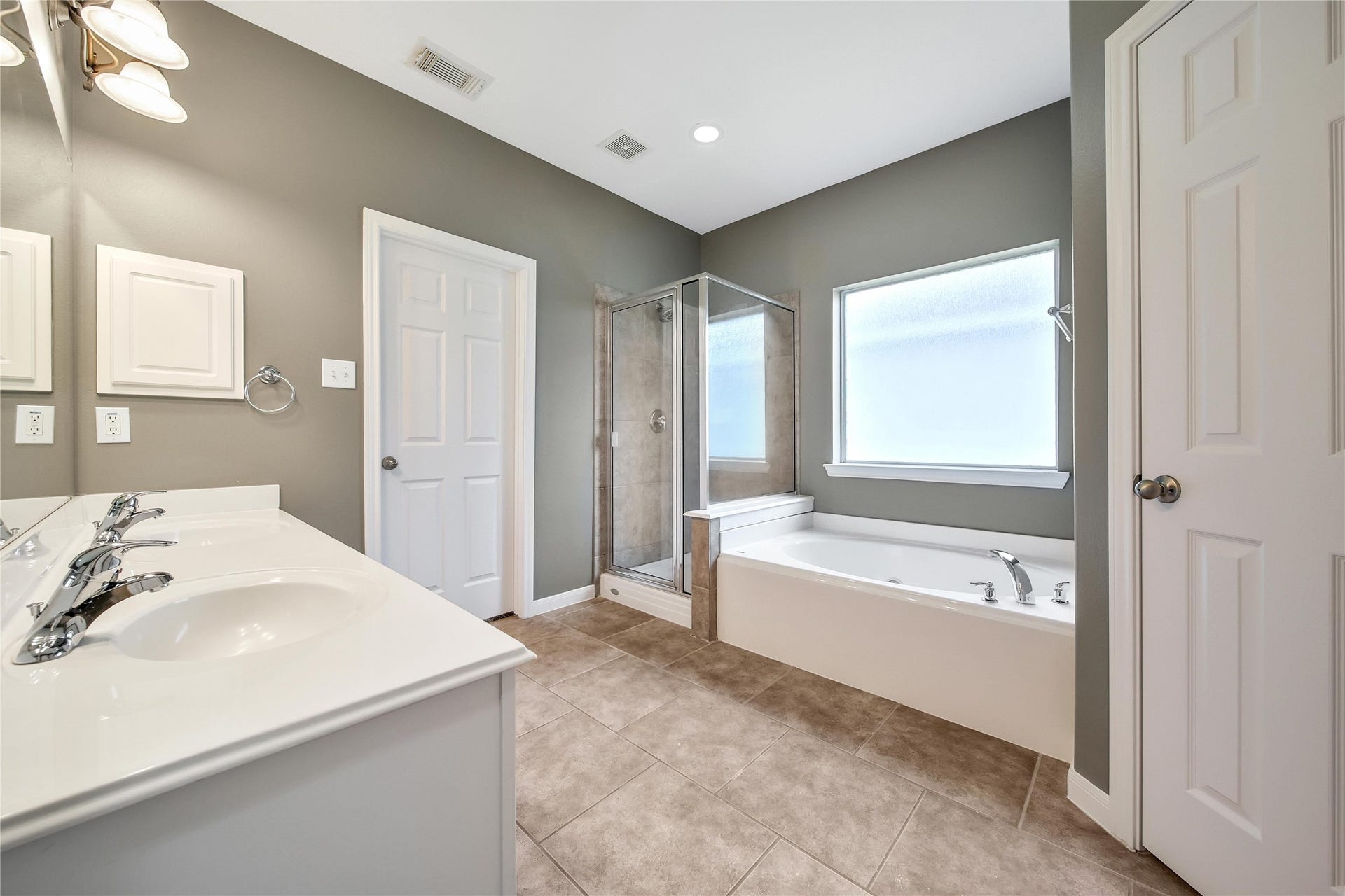 25604 Southwood Oaks Court, Porter, TX 77365 The modern looking primary bathroom features an oversized glass-enclosed shower, a separate bathtub, tiled flooring, and neutral wall colors. It includes a window for natural light, and a huge closet.