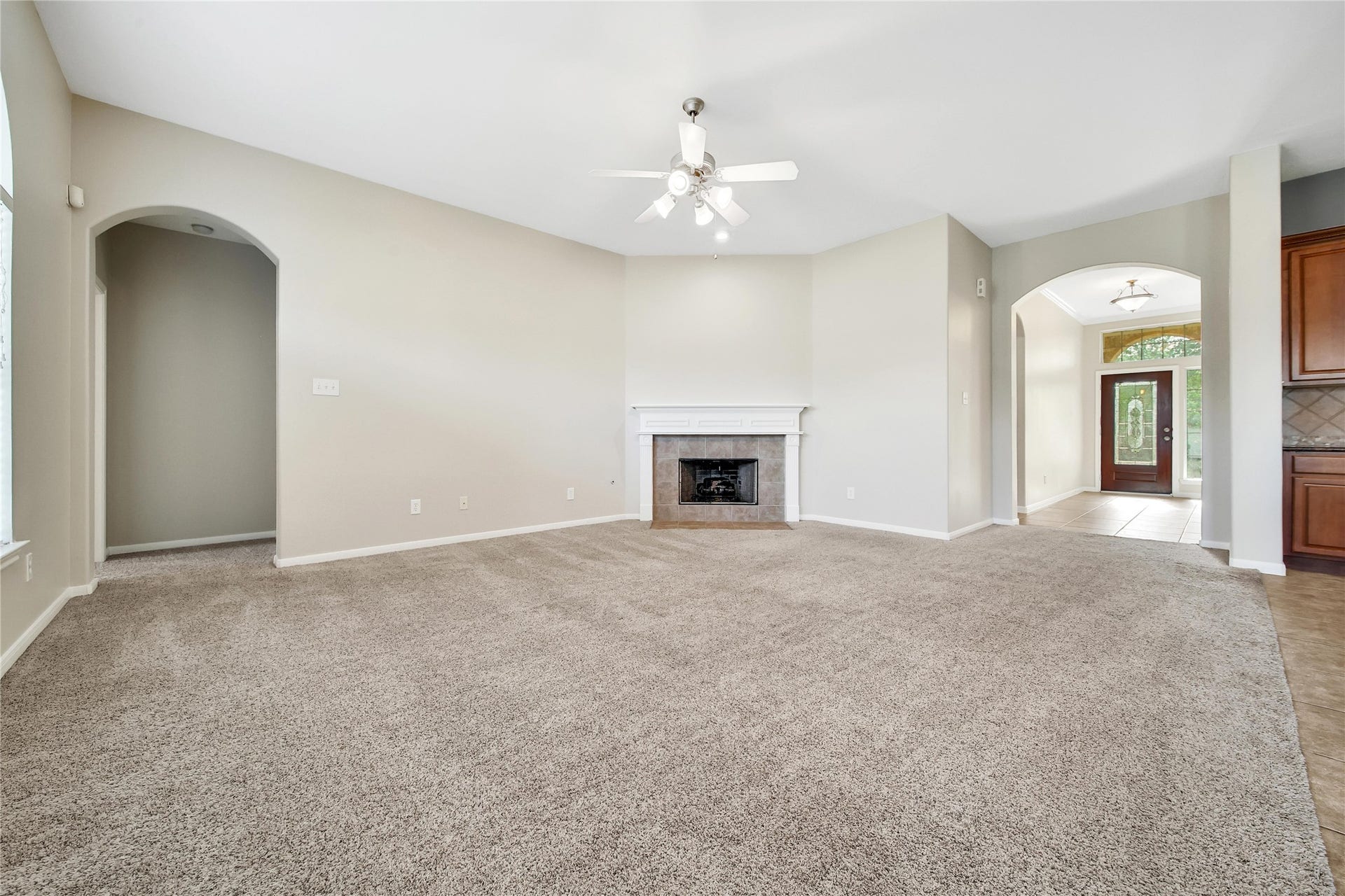25604 Southwood Oaks Court, Porter, TX 77365 This is a spacious, carpeted living room with a fireplace and high ceilings, featuring an arched doorway leading to the entry hall and another to the adjacent room, offering a bright and airy feel.