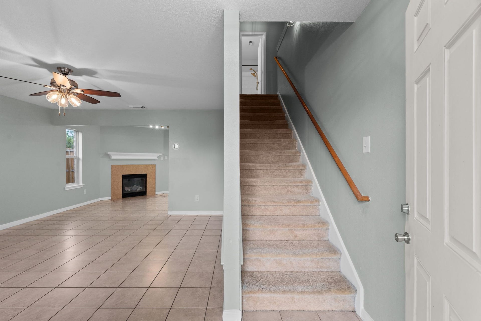 5800 Winding Brook Drive, Dickinson, TX 77539 Inviting living space with a cozy fireplace, ceiling fan, and tile flooring, adjacent to a carpeted staircase leading to the upper level.