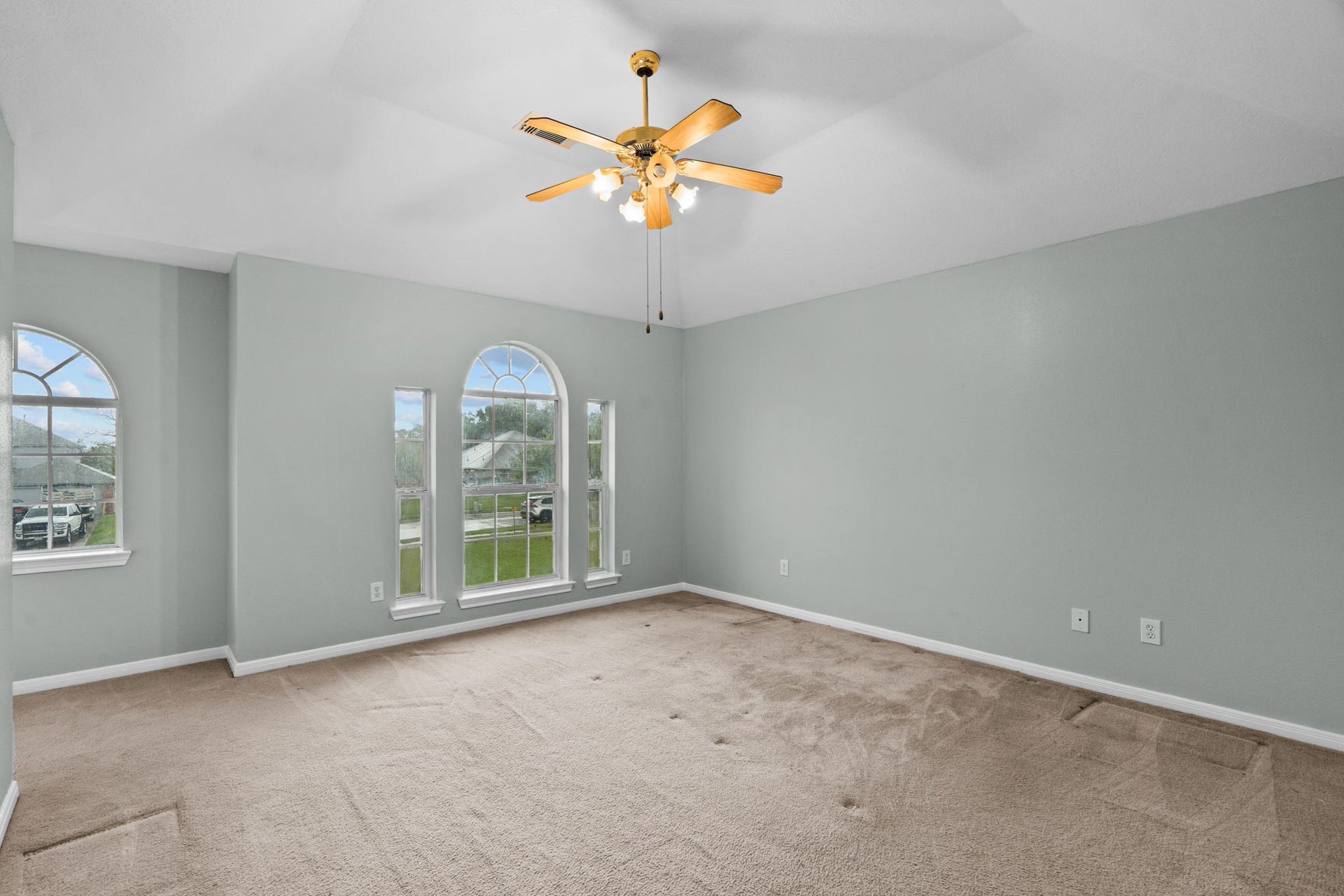 5800 Winding Brook Drive, Dickinson, TX 77539 Spacious room with vaulted ceilings, featuring large arched windows that provide ample natural light, complemented by soft carpeting and a ceiling fan for comfort.