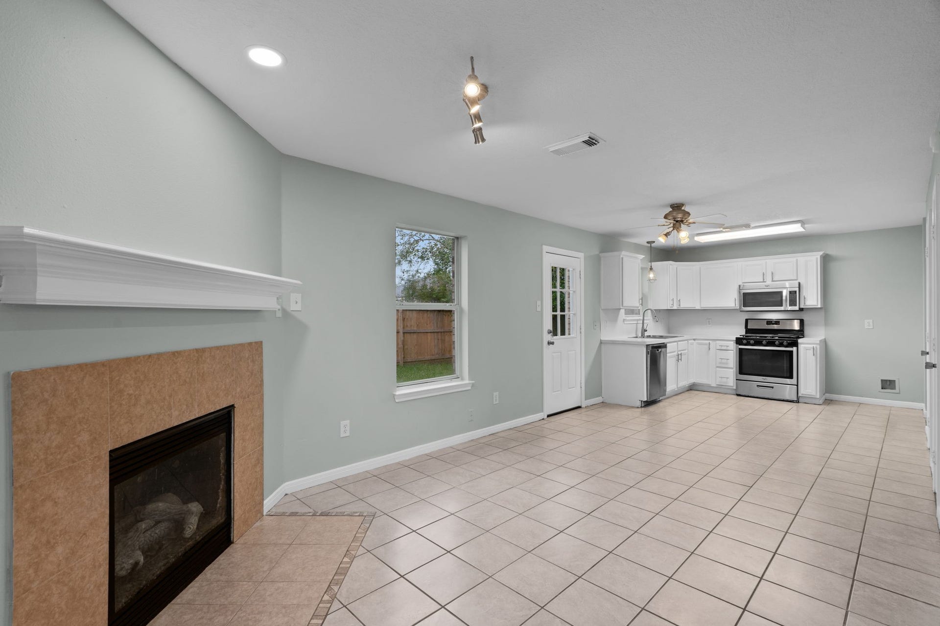 5800 Winding Brook Drive, Dickinson, TX 77539 Open-concept living area with a cozy fireplace, light tile flooring, and modern kitchen featuring stainless steel appliances and white cabinetry.