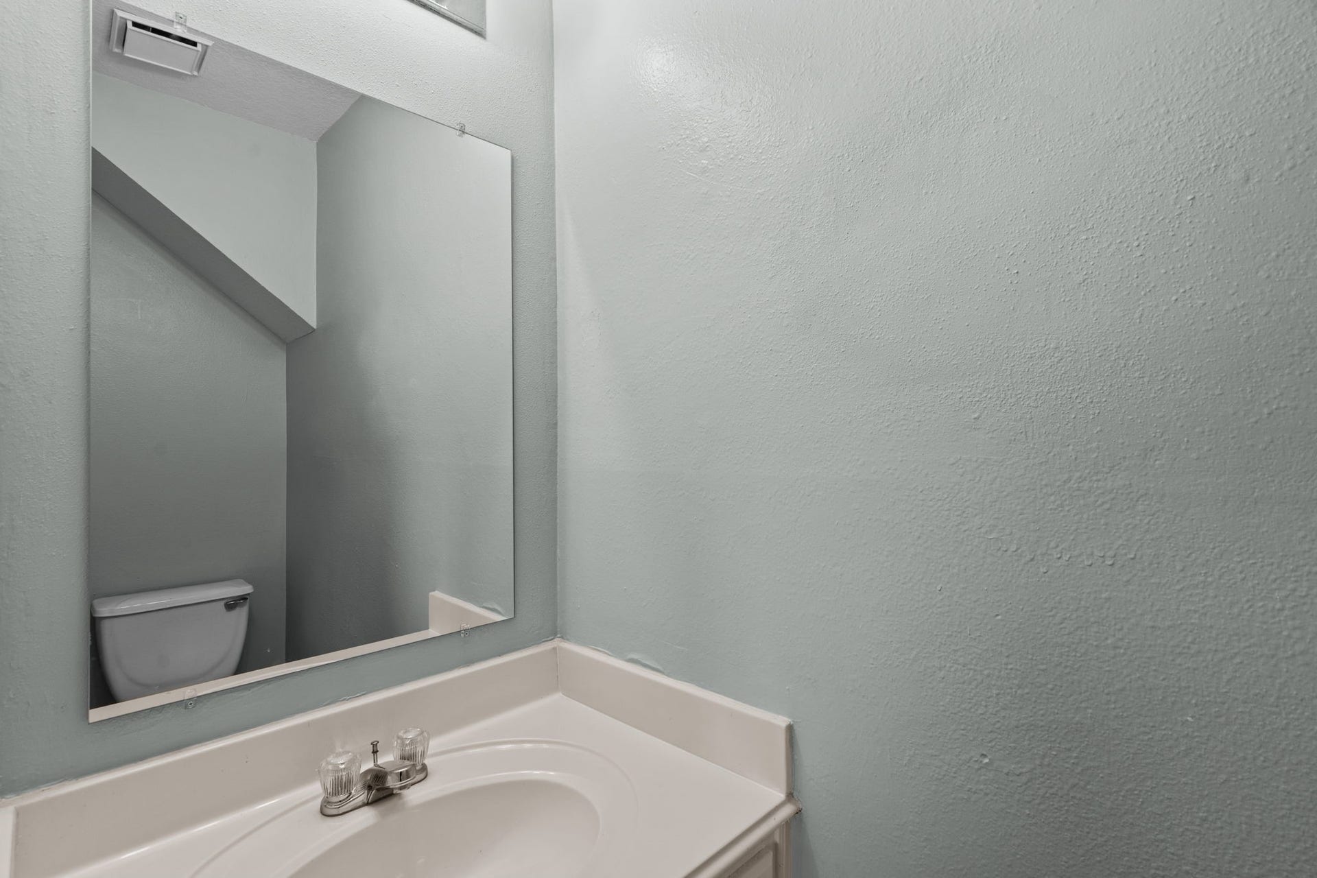 5800 Winding Brook Drive, Dickinson, TX 77539 Compact half-bathroom with a sleek mirror, modern sink, and soft gray walls.