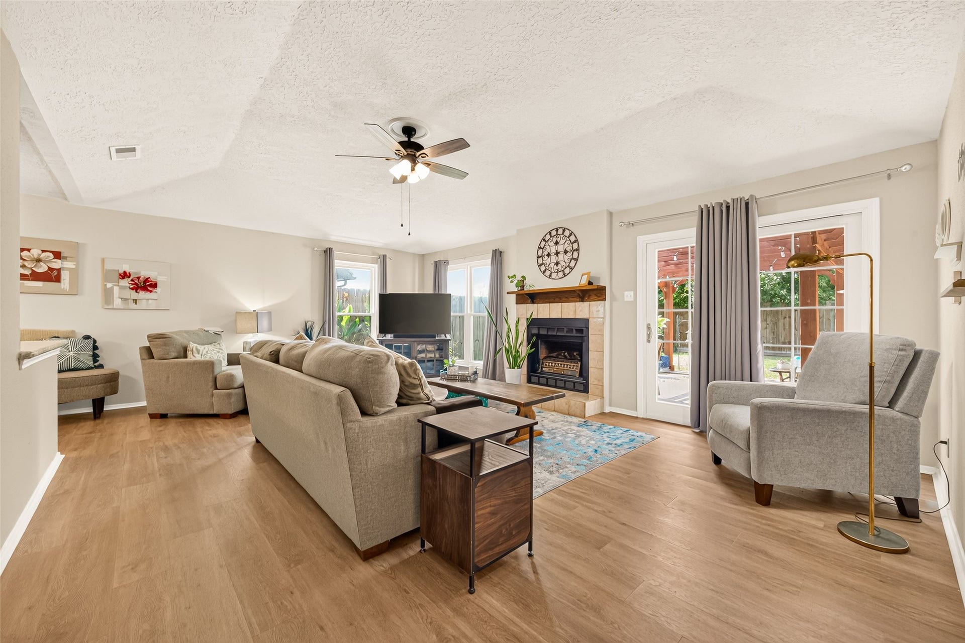 2123 Collingsfield Drive, Sugar Land, TX 77478 Spacious living room with cozy fireplace, abundant natural light from large windows and newer glass doors leading to the patio, complemented by elegant wood flooring and neutral-toned furnishings.