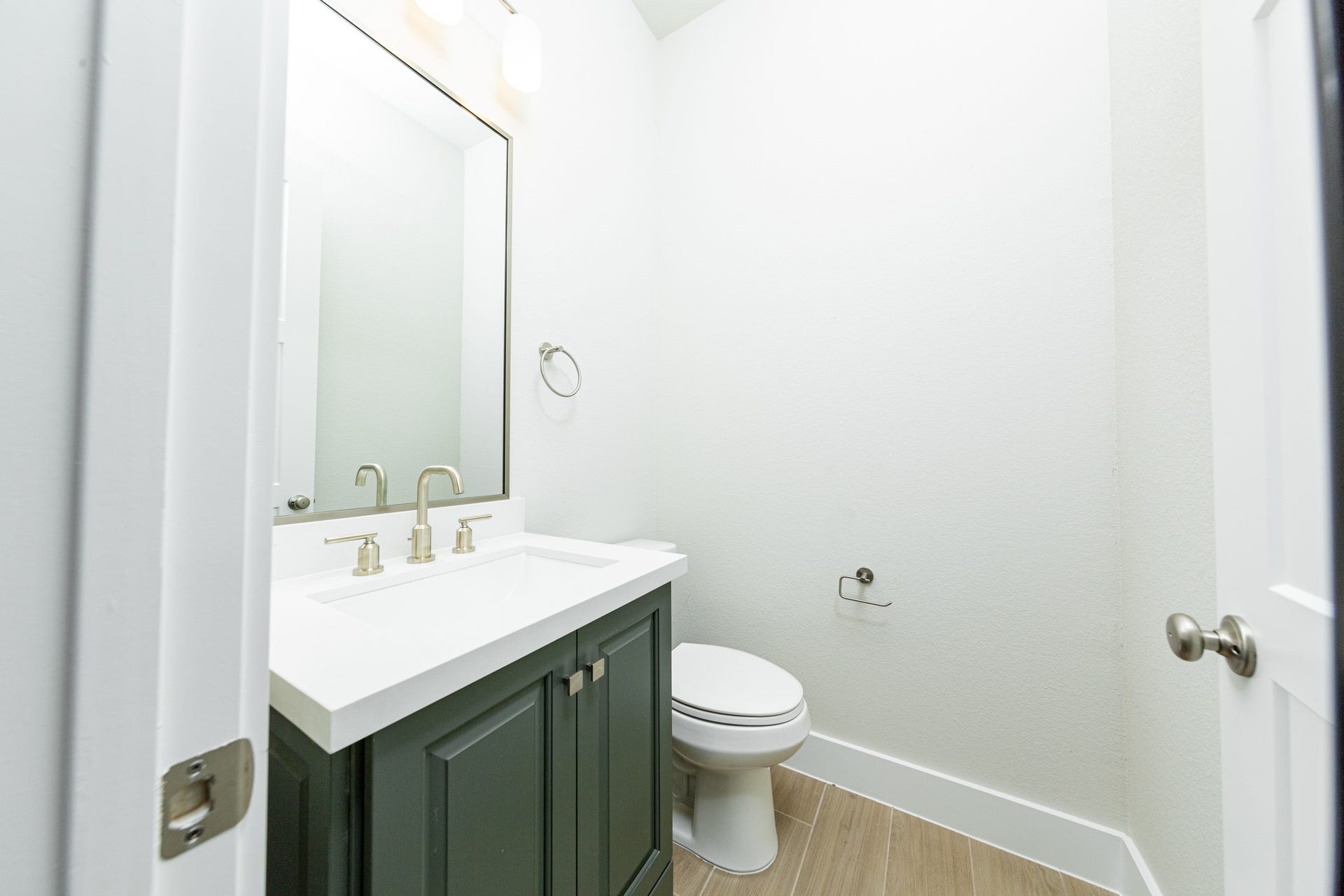 1915 Langford Street, Montgomery, TX 77316 The powder room offers convenience and a modern aesthetic. It features a stained cabinet with quartz countertop and brushed nickel fixtures, matching wall-mounted towel ring, and a simple, large rectangular mirror.