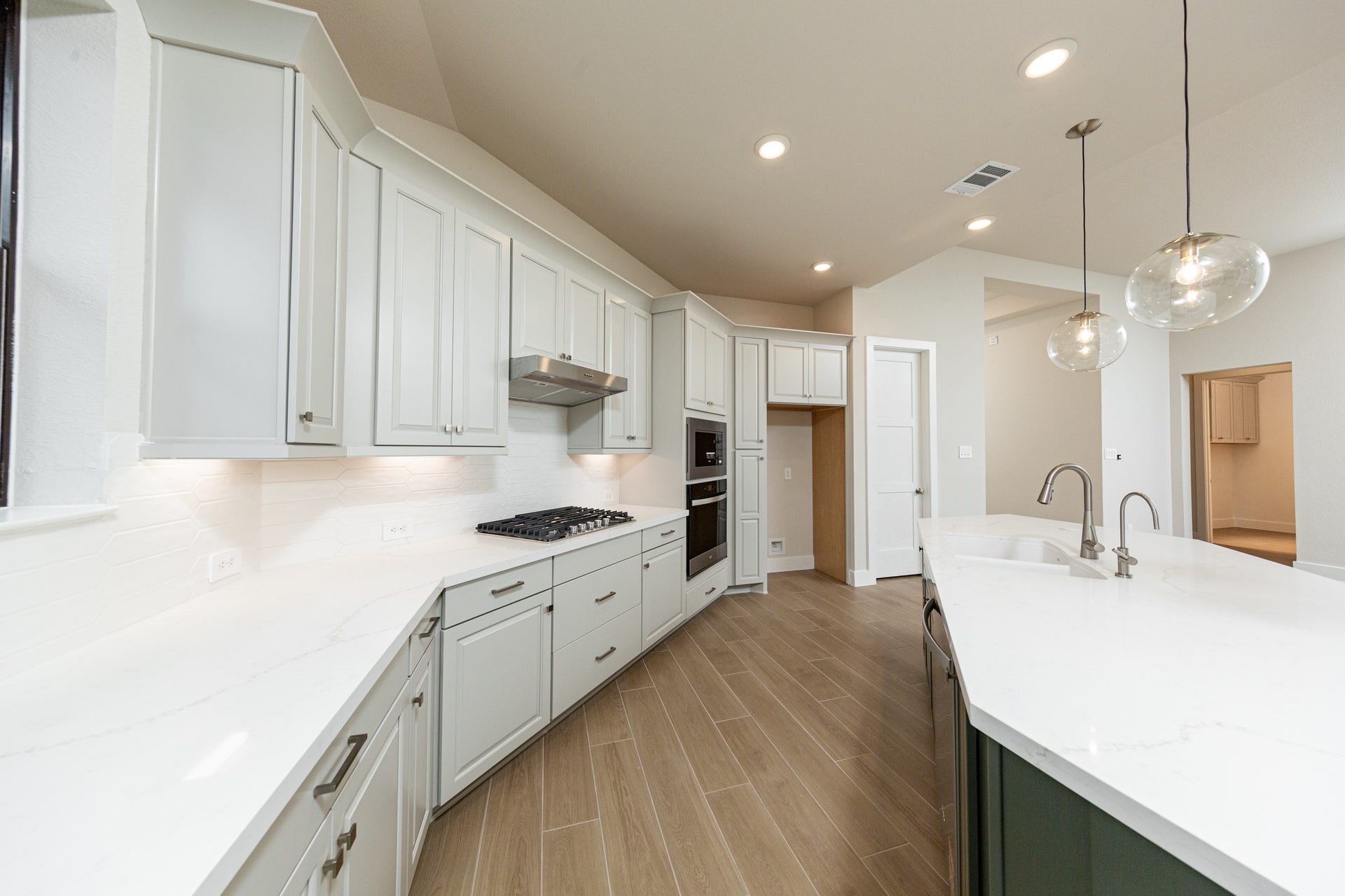 1915 Langford Street, Montgomery, TX 77316 The open-concept gourmet kitchen designed for both cooking and entertaining. It features elegant white cabinetry, pristine quartz countertops, and a large central island that doubles as a functional breakfast bar. Three glass pendants elegantly hang above the kitchen island, providing focused task lighting and a touch of refined style.