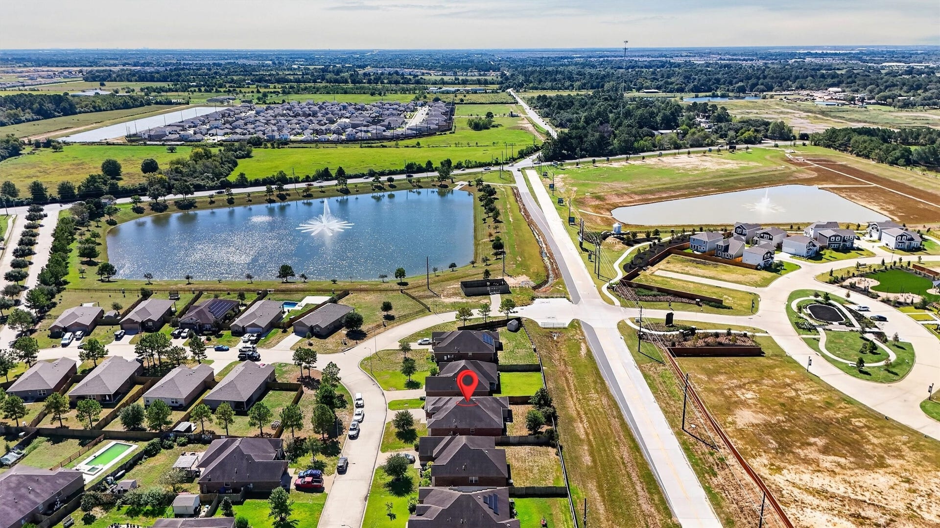 22907 Gentle Shadow Drive, Hockley, TX 77447 A fresh perspective on a welcoming neighborhood! This aerial view highlights the homes location along a curved residential street, with no home directly behind the property. A nearby pond with a striking fountain, tree-lined edges, and surrounding green space adds scenic appeal. The wider view showcases the neighborhood layout and surrounding area, giving you a sense of where your next chapter could begin.
